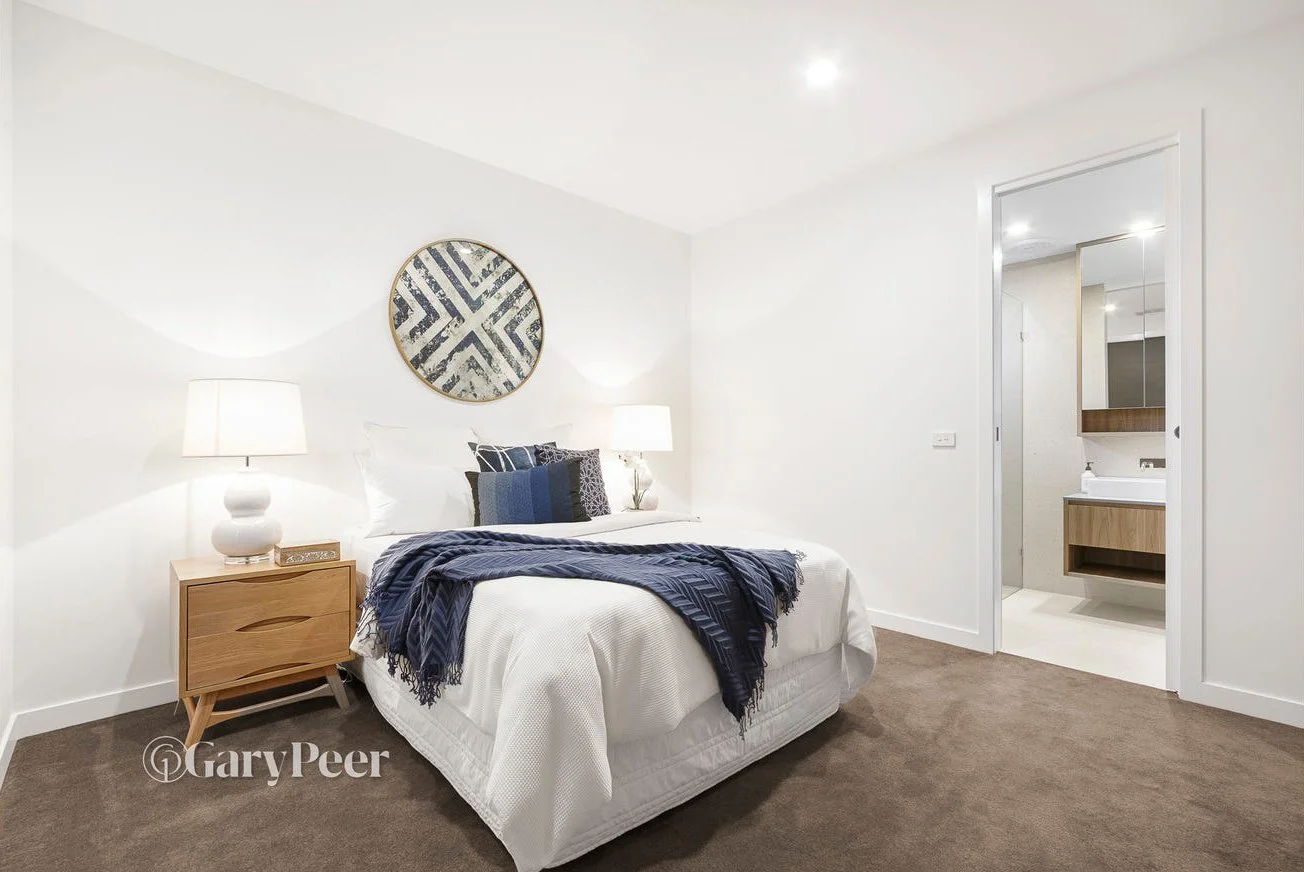 Bedroom with a bed, nightstand, lamps, and artwork, adjacent to a bathroom with a vanity, mirror, and sink.