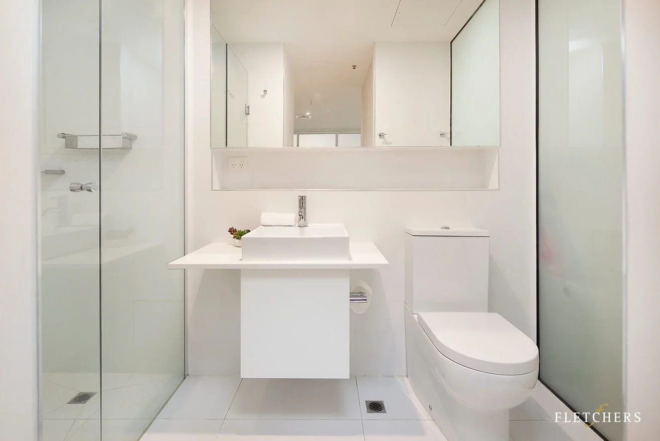 Modern white bathroom with a sink, toilet, mirror, and shower with glass doors.