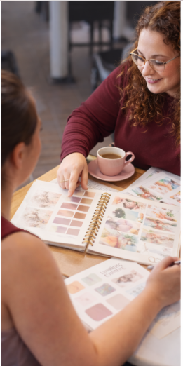 Two women at coffee shop with planning books and style boards,