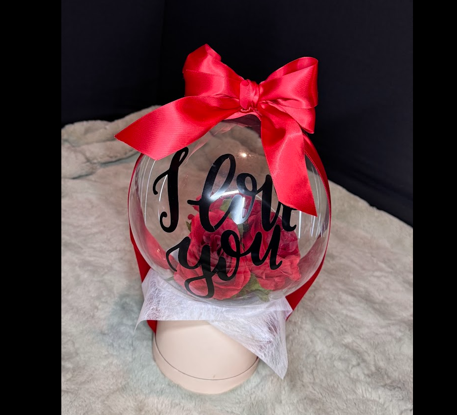 Valentine's Daystuffed bubble balloon with roses, placed in a flower box, tied with a pink ribbon and "I love you" wording. 