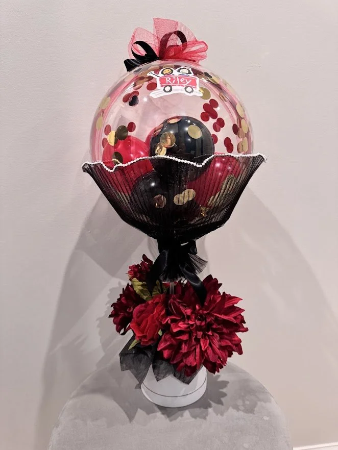 Custom Riley Hospital Themed Piece - Stuffed Bubble Balloon with black and red balloons and confetti. On a stand in a flower box, overflowing with red flowers. 