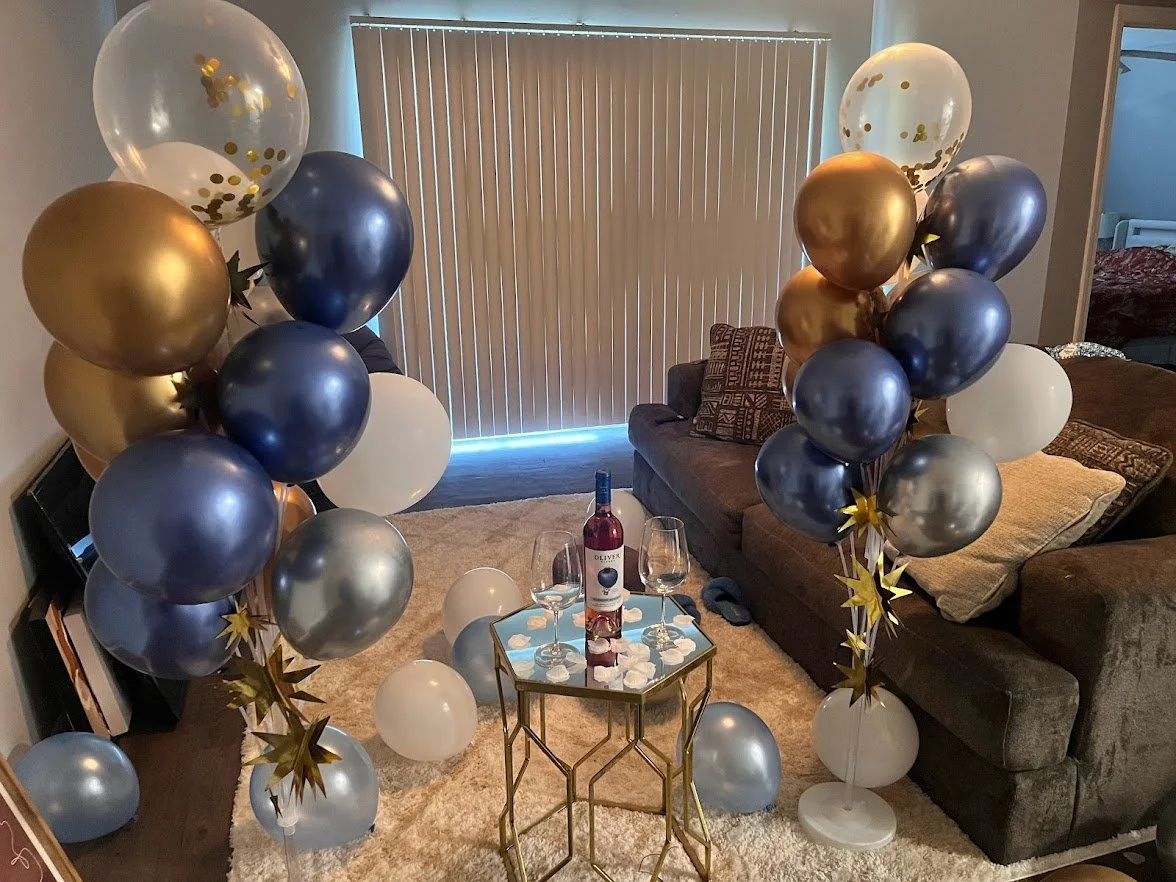 Balloon bouquets with navy, gold, and confetti balloons, staged with a table and wine, with balloons scattered throughout 
