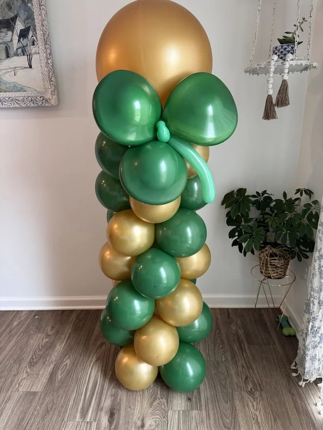 A tall column of green and gold balloons with a large green balloon topper shamrock.