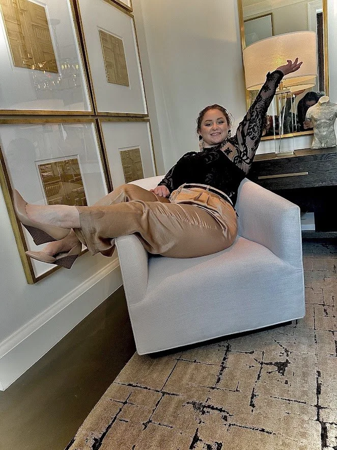 Owner of Velvet Curl Events relaxing in a chair in a stylish interior, smiling with arm raised.