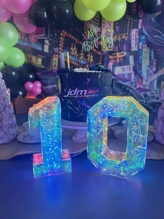 Theme Development - Japanese Domestic Market (JDM), with neon and black street car backdrop, surrounded by a full organic garland of Neon and Black balloons, Happy Birthday LED Sign, and blue neon strip intertwined in the balloons, and iridescent num