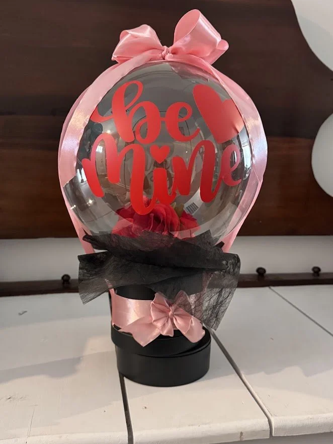 Valentine's Day stuffed bubble balloon with roses, placed in a flower box, tied with a pink ribbon and "be mine" wording. 