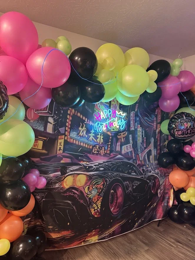 Theme Development - Japanese Domestic Market (JDM), with neon and black street car backdrop, surrounded by a full organic garland of Neon and Black balloons, Happy Birthday LED Sign, and blue neon strip intertwined in the balloons. 