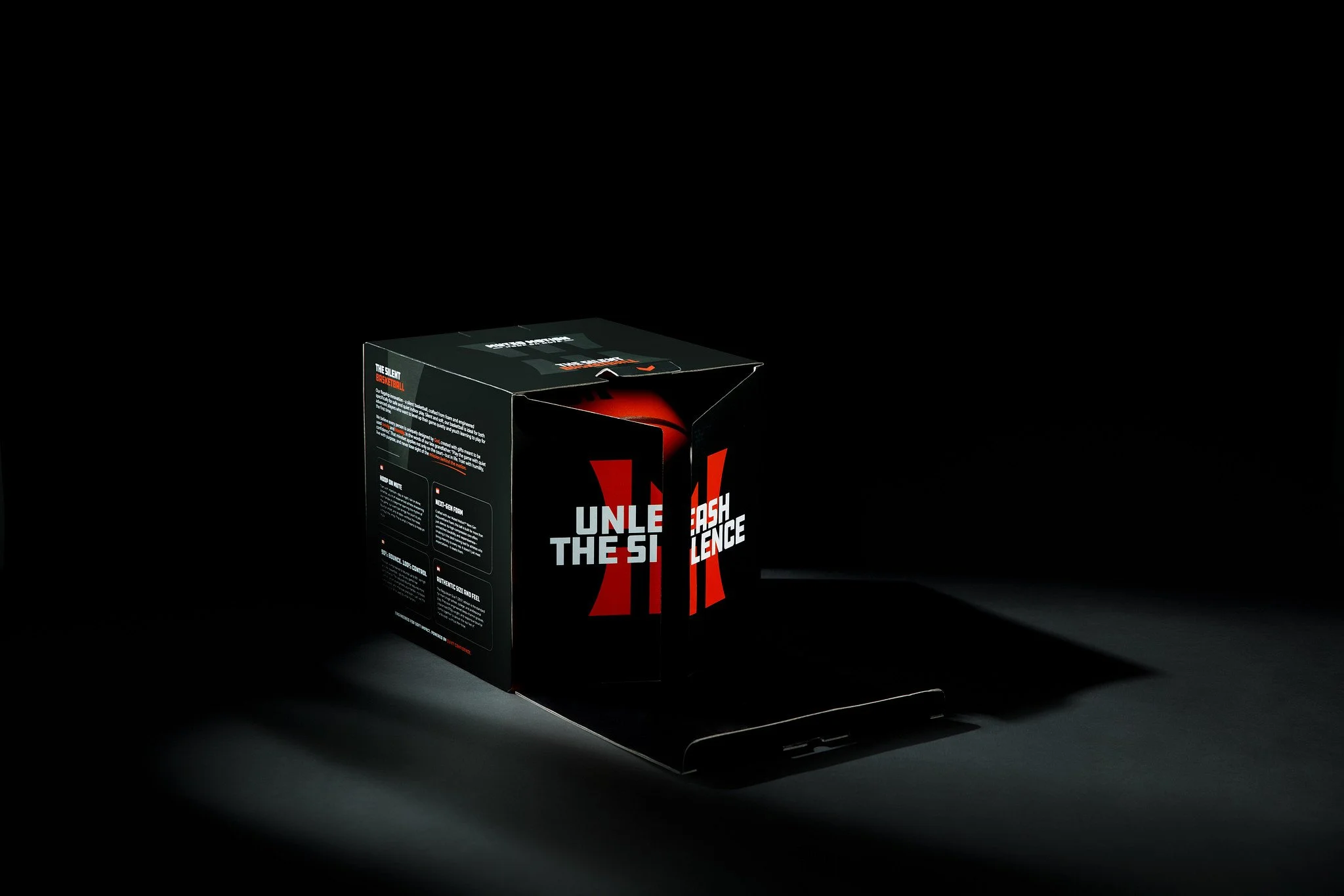 Box for a basketball training product with bold red and white text, partially pulled open, on a black surface with a dark background.