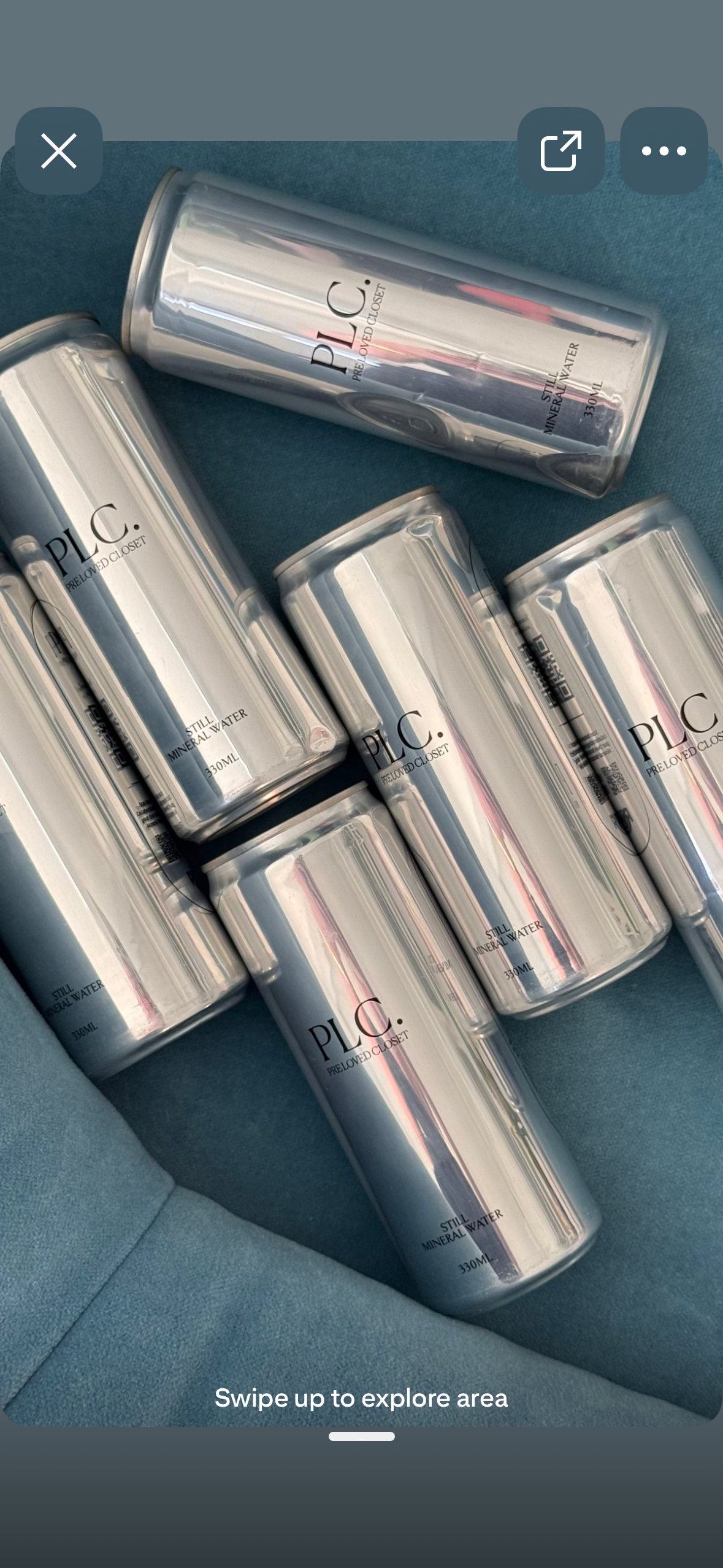 Several silver canned drinks labeled 'PLC. Preloved Closet, Still Mineral Water, 330ML' are arranged on a blue fabric surface.