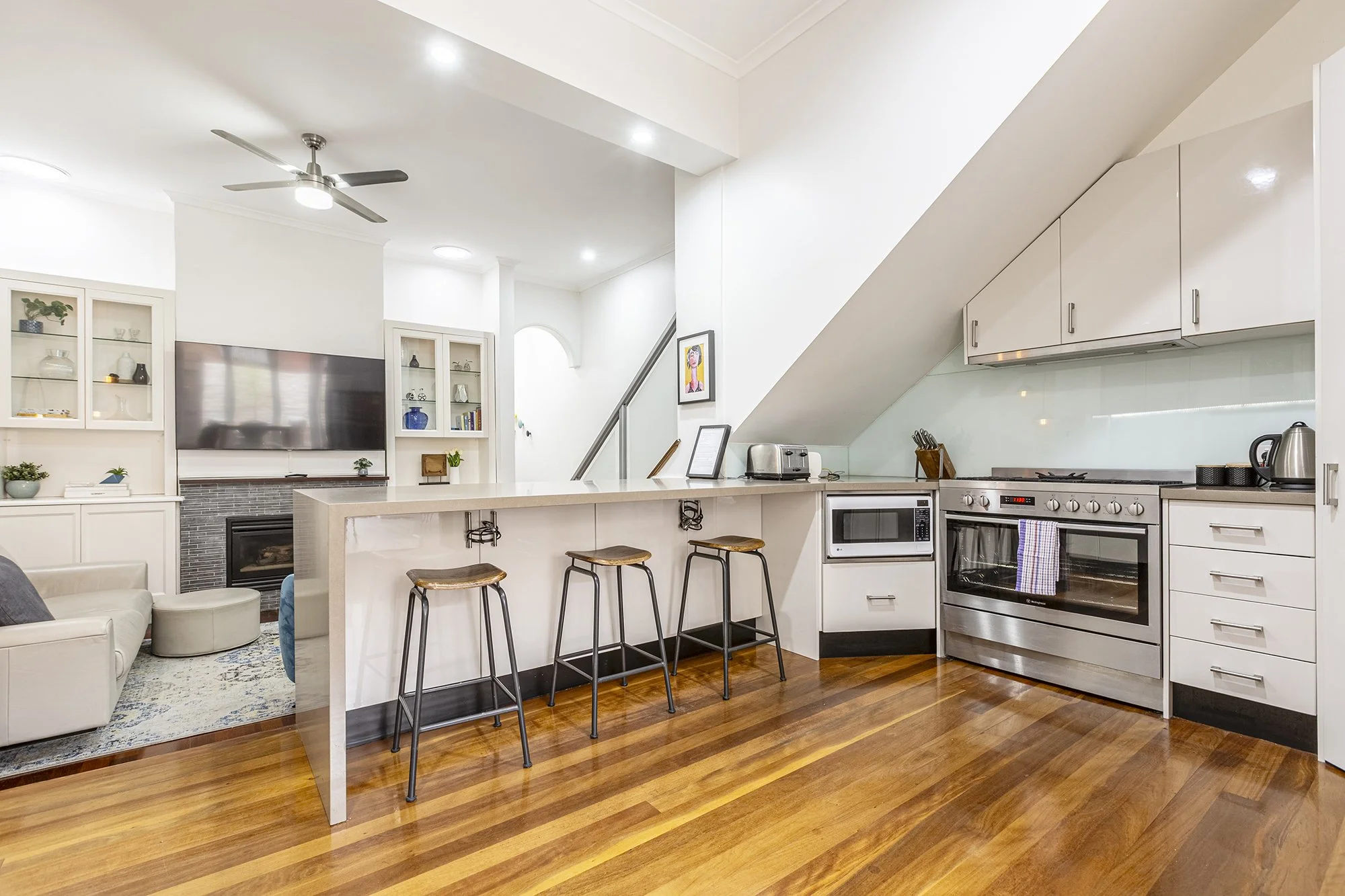 Open-plan kitchen and living area in a North Melbourne Airbnb, showing full room coverage from stove to lounge in one wide shot
