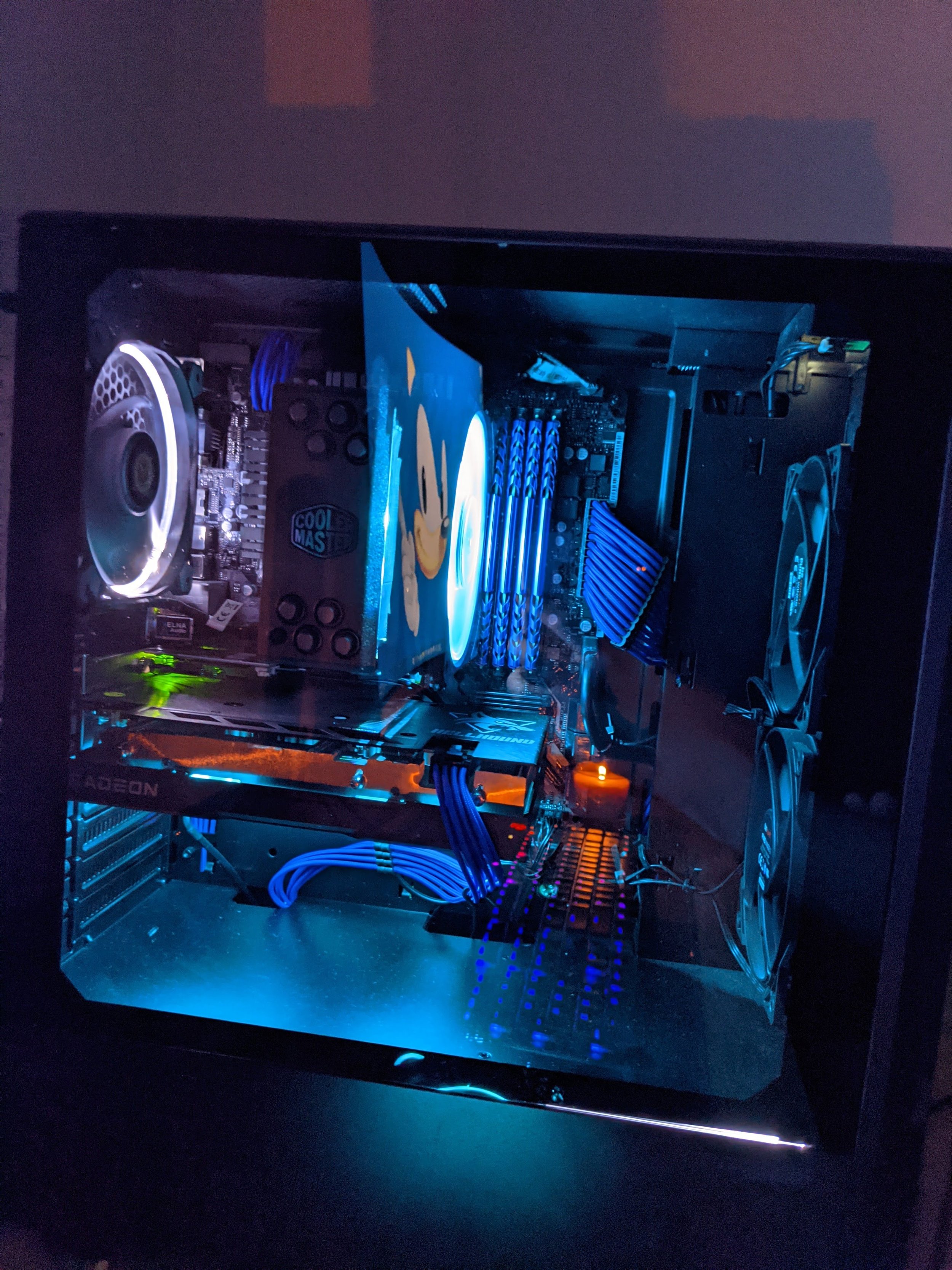 Inside a gaming or high-performance computer with illuminated components, including a cooling fan, graphics card, RAM sticks, and a CPU cooler, all set in a black case with a glass side panel.