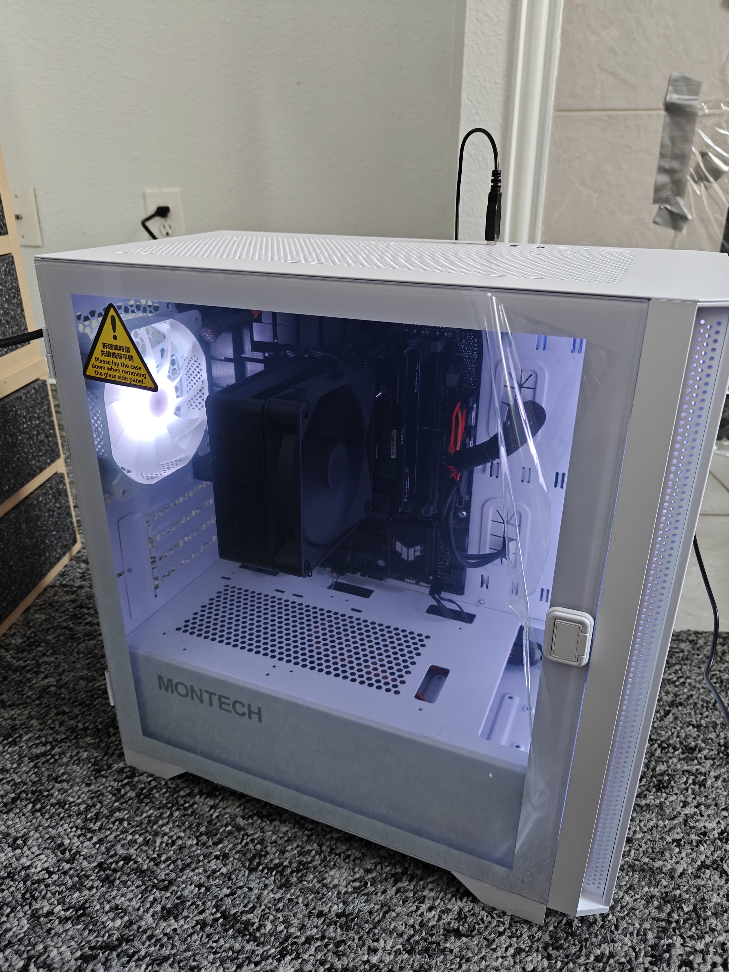 A white Montech computer case with a tempered glass side panel showing the internal components, including a cooling fan, CPU cooler, and various cables.