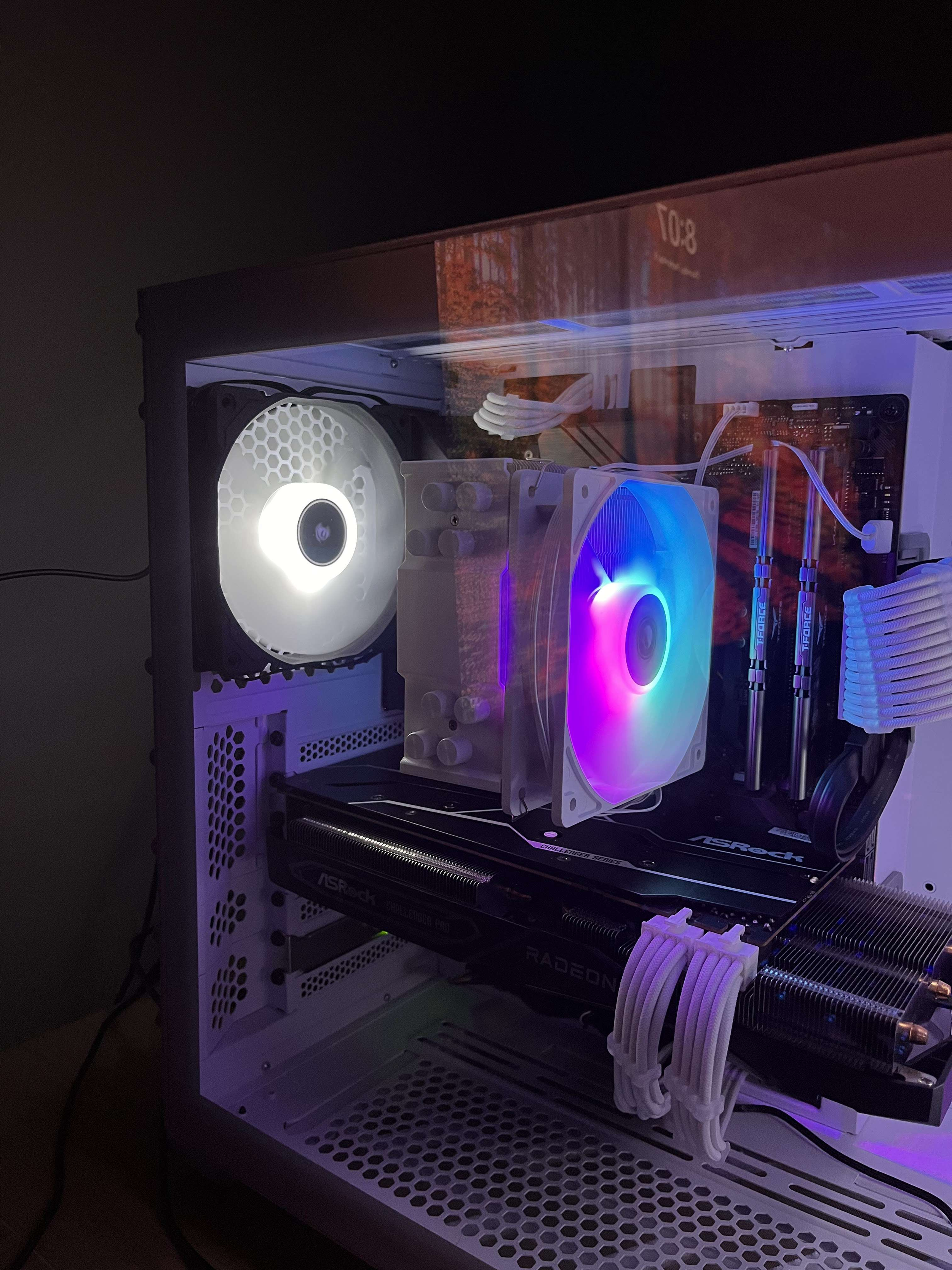 Inside a custom white gaming computer with RGB lighting, featuring a CPU cooler, graphics card, case fans, and cables visible through a transparent side panel.