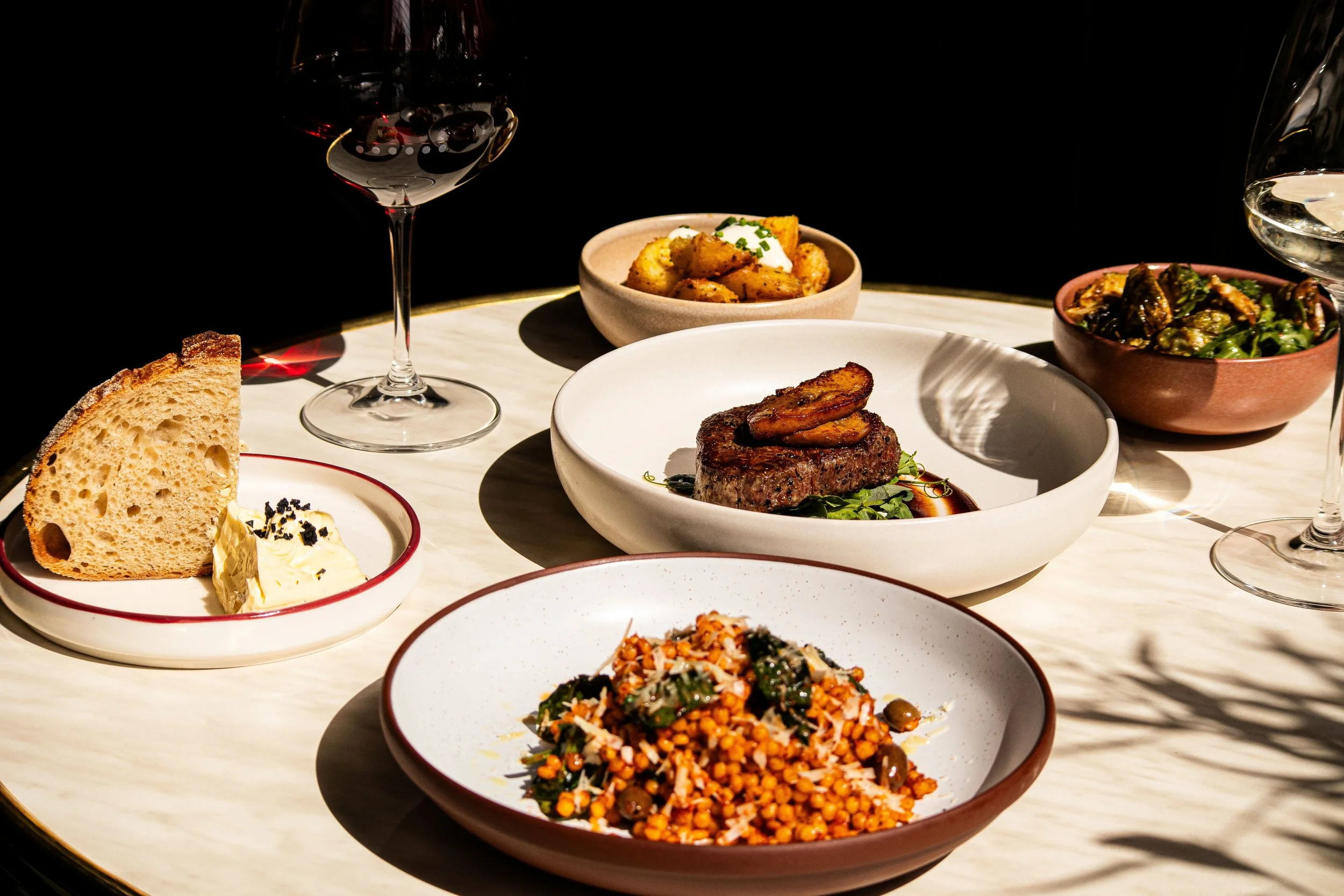Various dishes of food on a table with glasses of red and white wine for Sunday Date Night at Annabel's Wine Bar