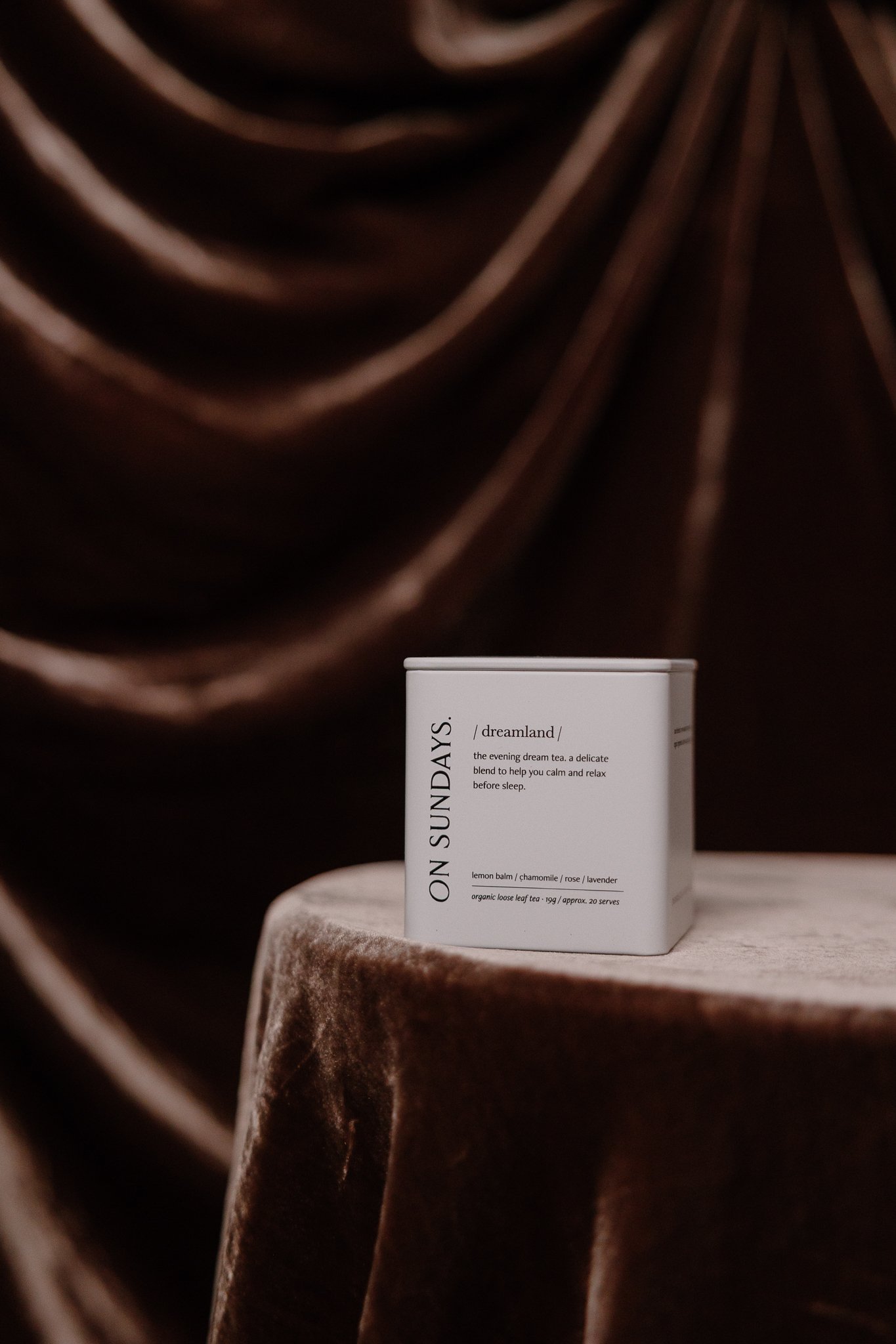 A person wearing a long white dress and a matching white sweater, holding the dress with one hand, standing against a beige wall.