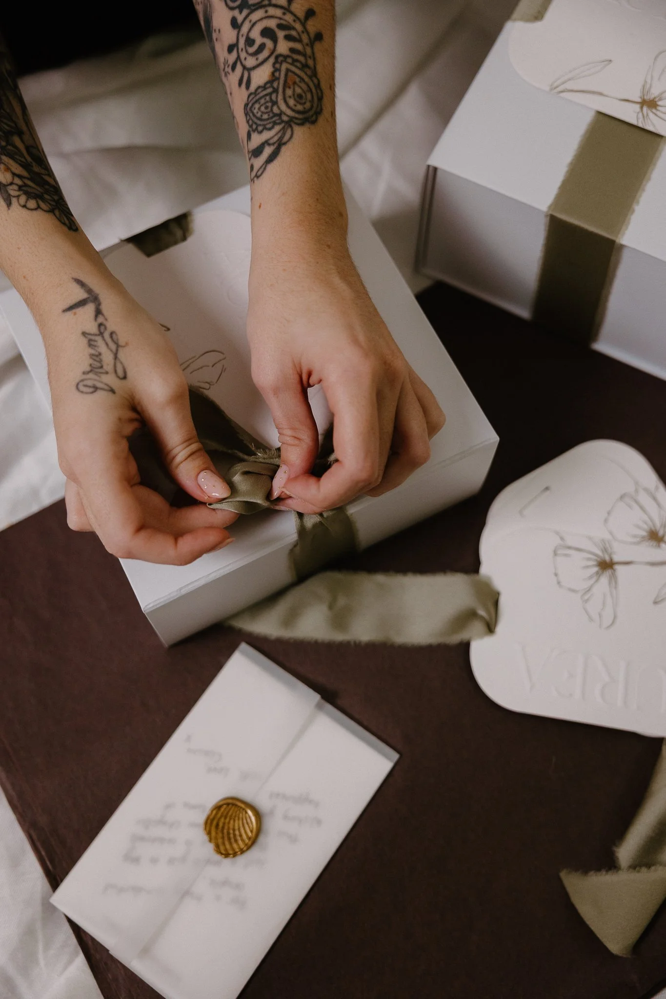 White folded paper with a decorative wax seal featuring a leaf, placed upright against a folded yellow paper on a neutral surface.