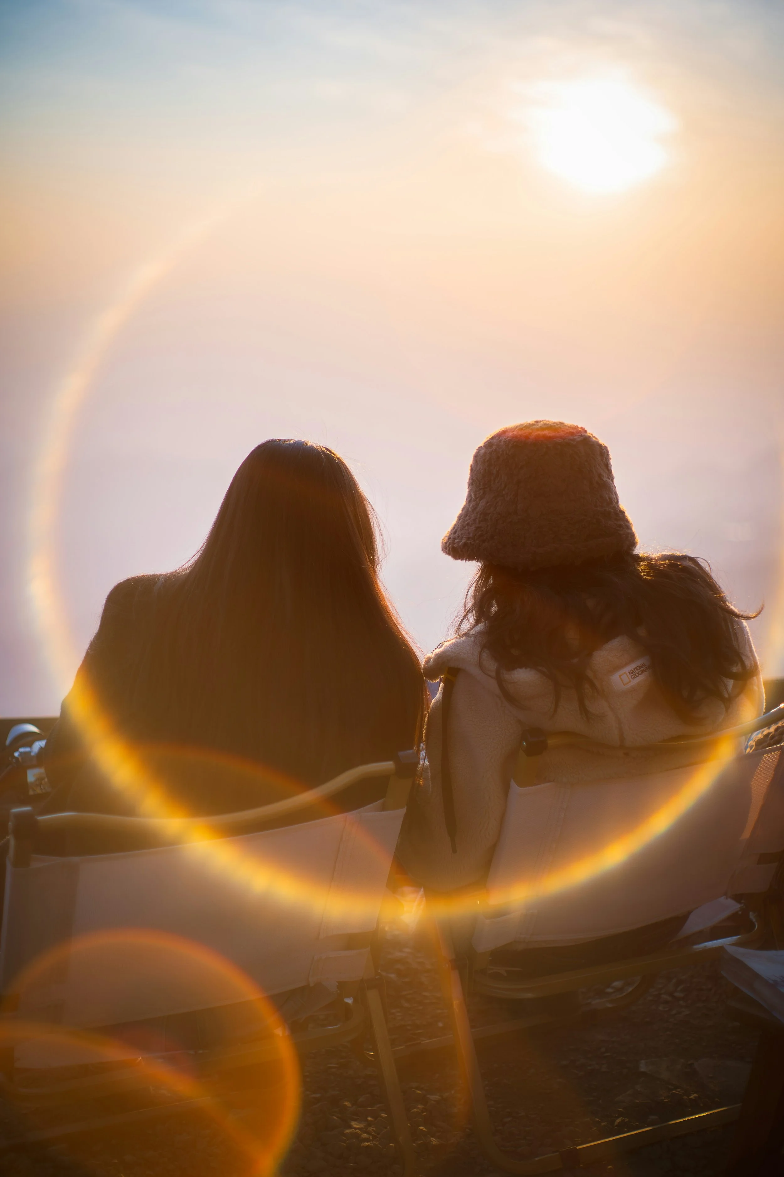 Two people sitting on a wooden pier or dock at dusk, looking out at the ocean under a cloudy sky.