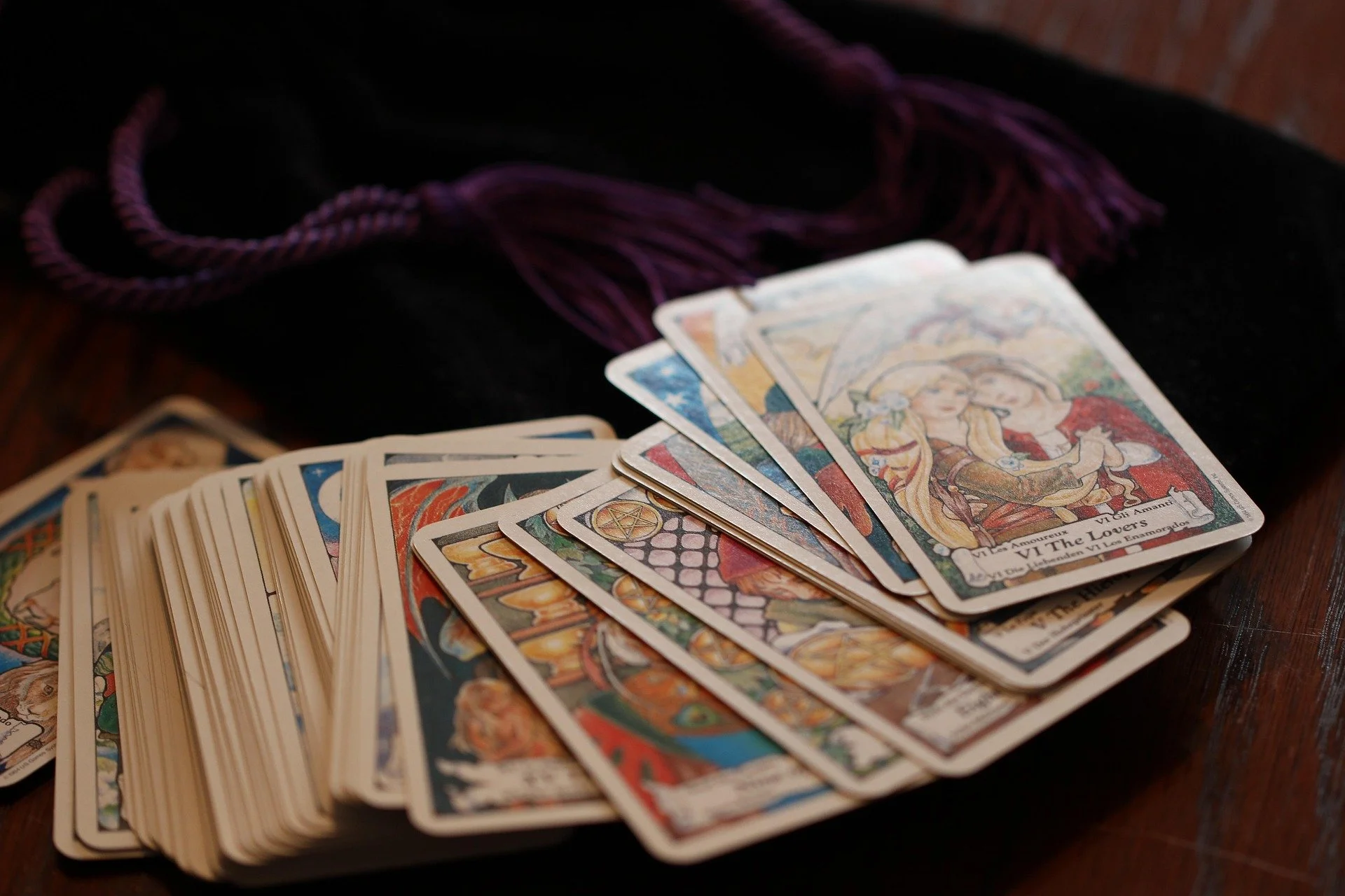 Fanned spread of tarot cards with colorful illustrations on a dark surface with purple tassel in the background.
