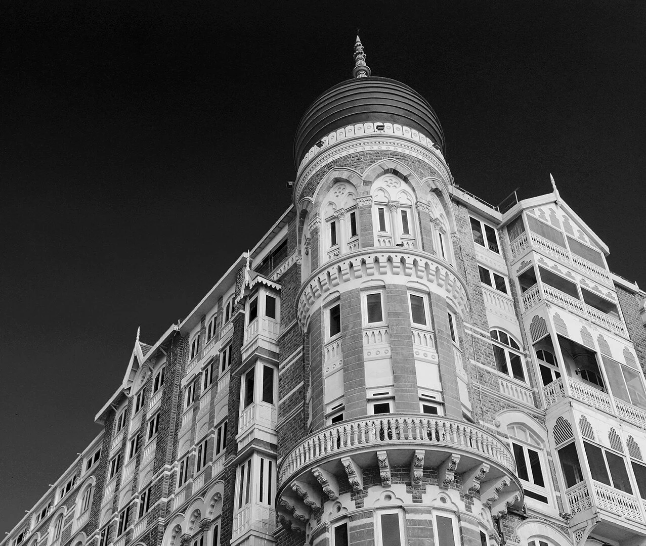 Black and white photo of a historic multi-story building with ornate architectural details and a rounded turret topped with a spire.