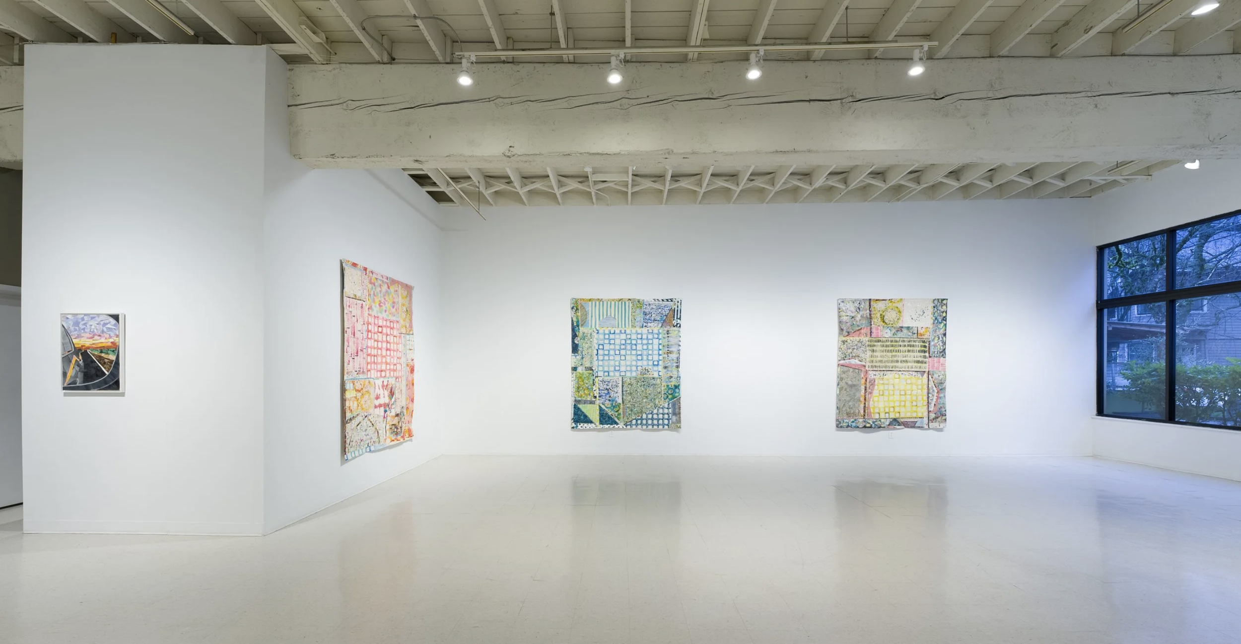 Art gallery in Portland Oregon or New York City with white walls displaying five textile art pieces from Whitney Nye and a large window showing trees outside.