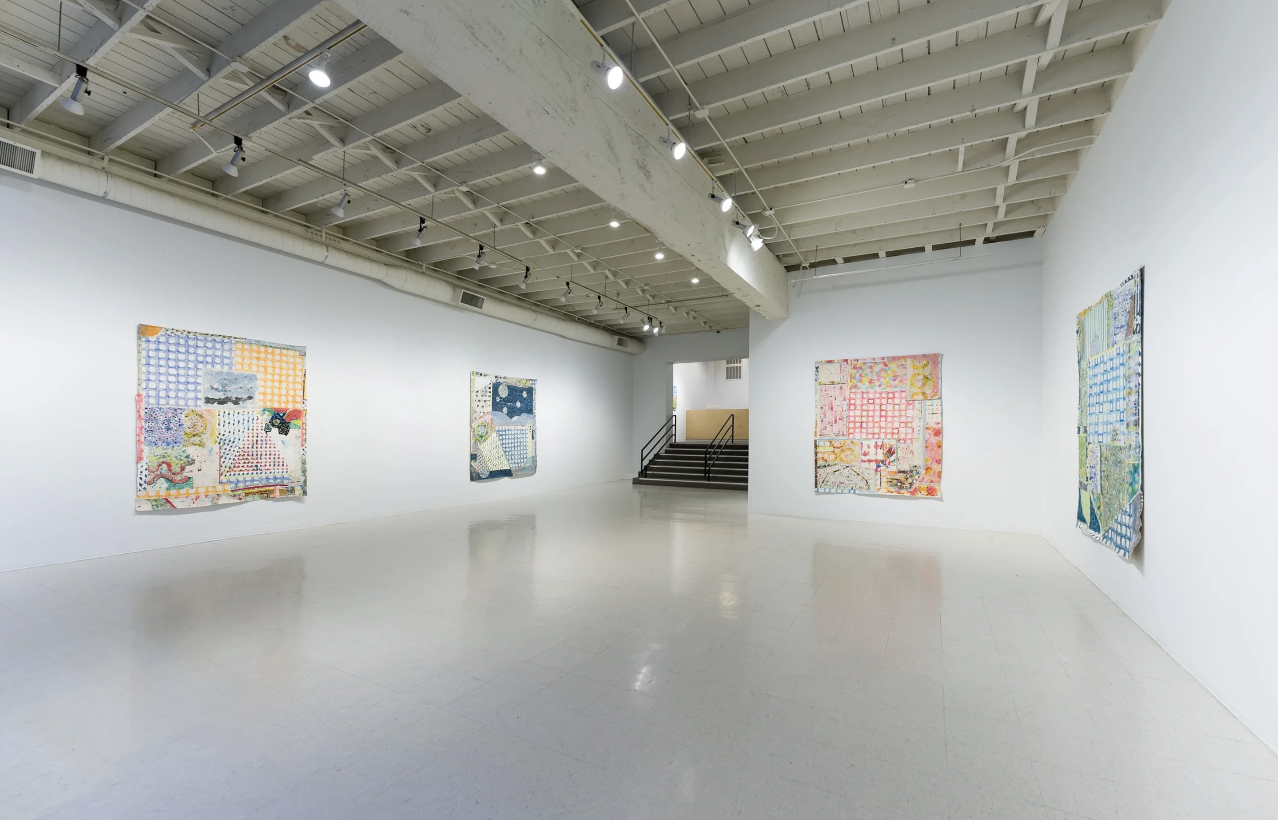 Art gallery with white walls displaying several colorful, abstract textile artworks.