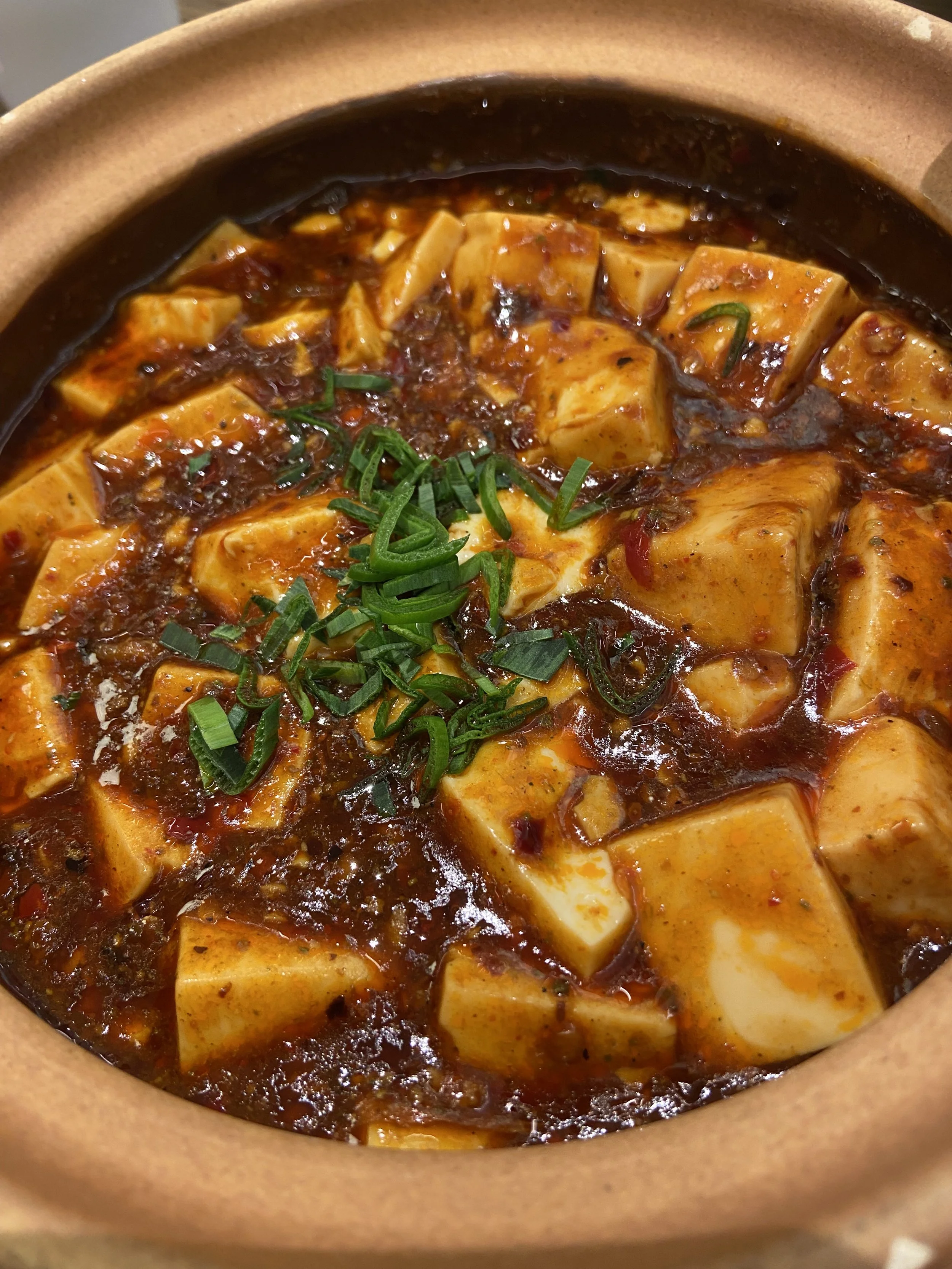 A bowl of spicy tofu stew garnished with chopped green onions.
