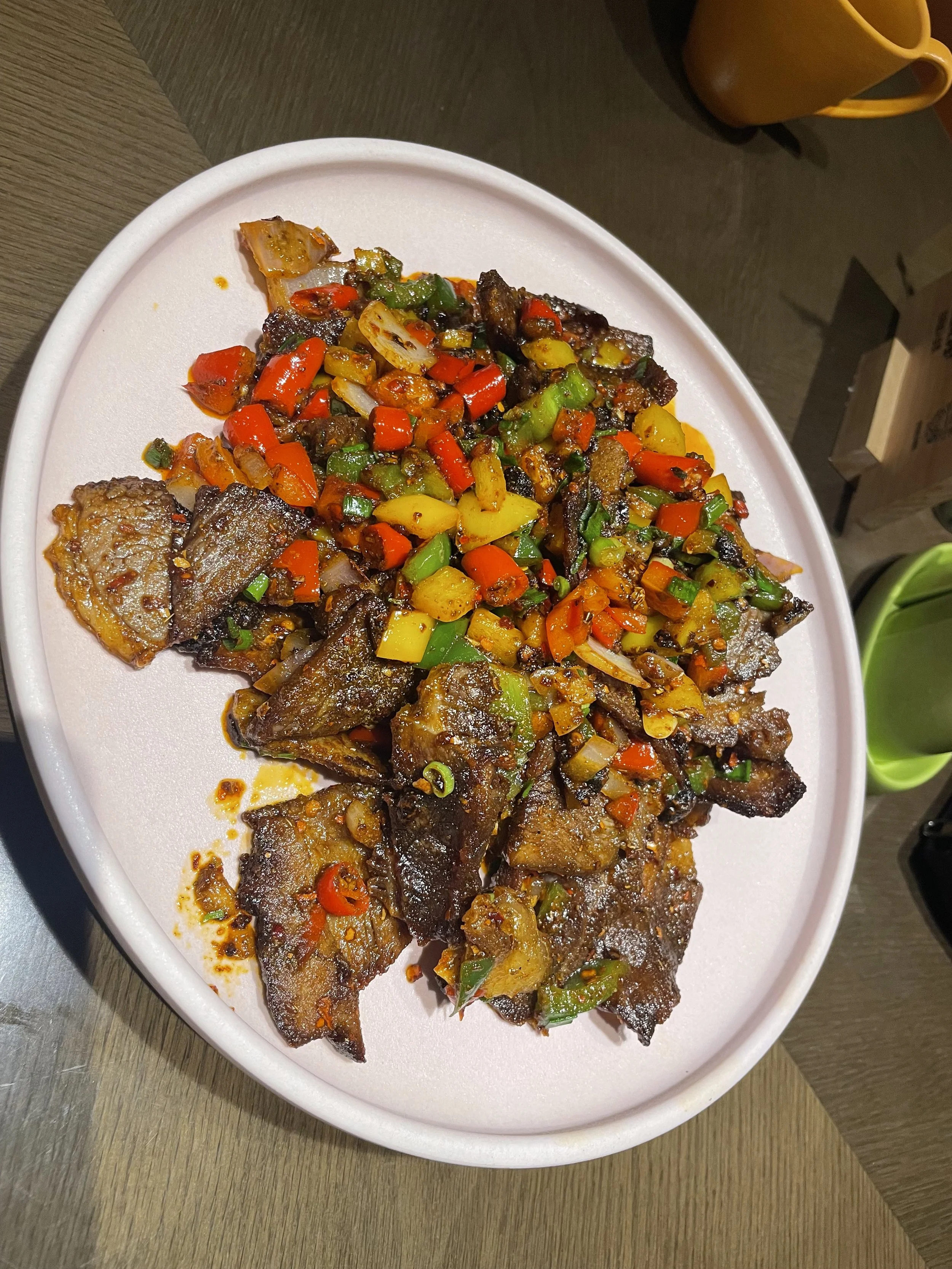 Fried fish fillets topped with sautéed chopped red, green, and yellow bell peppers on a white oval plate.