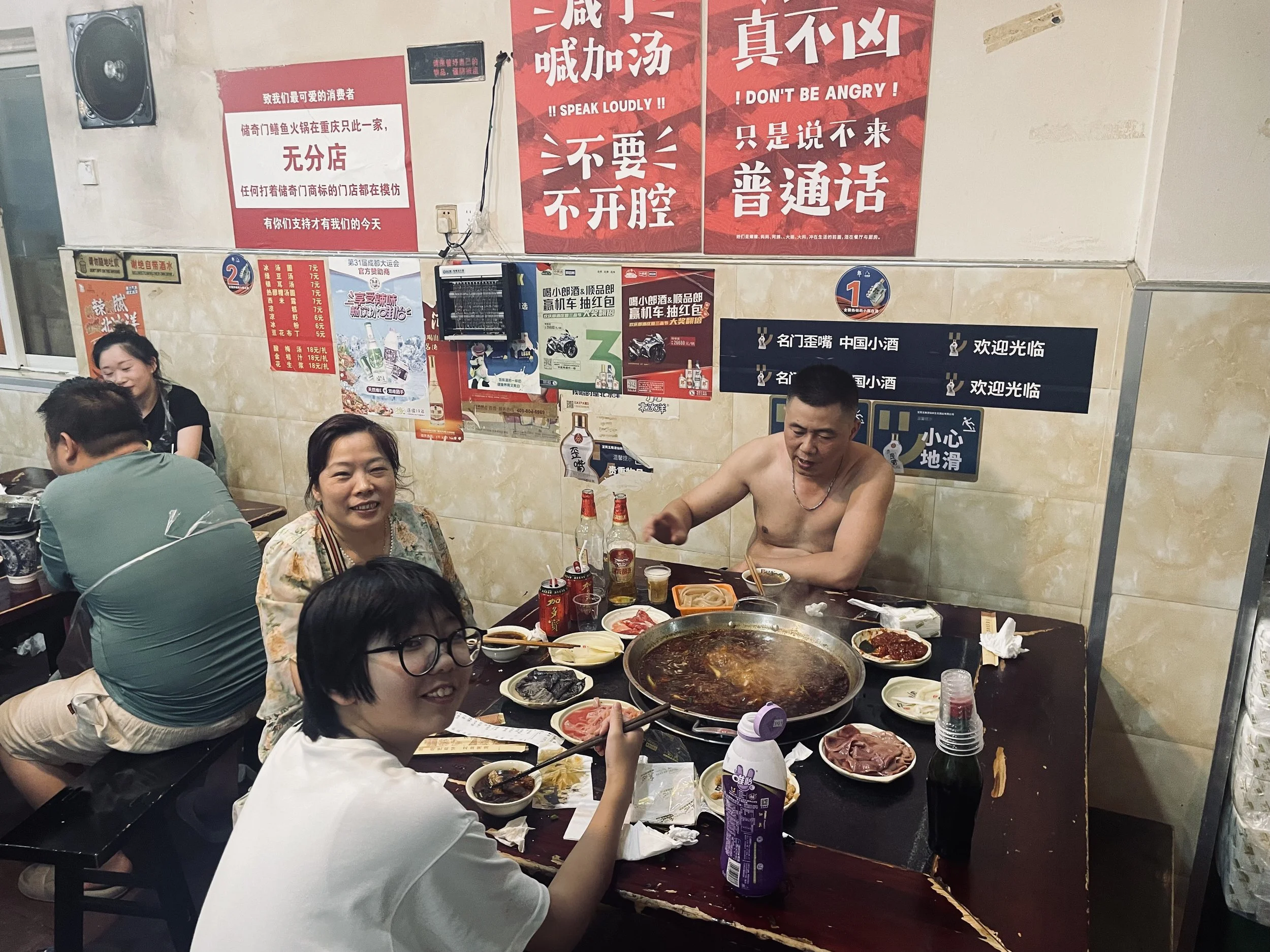 People enjoying a hotpot meal in a Chinese restaurant with red and black Chinese and English signs on the wall.