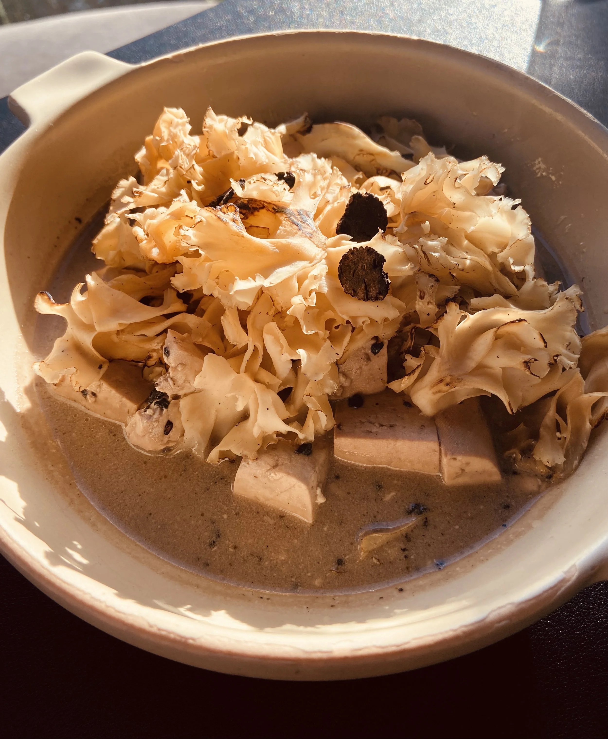 A bowl of mushroom soup topped with fresh mushrooms and black pepper.