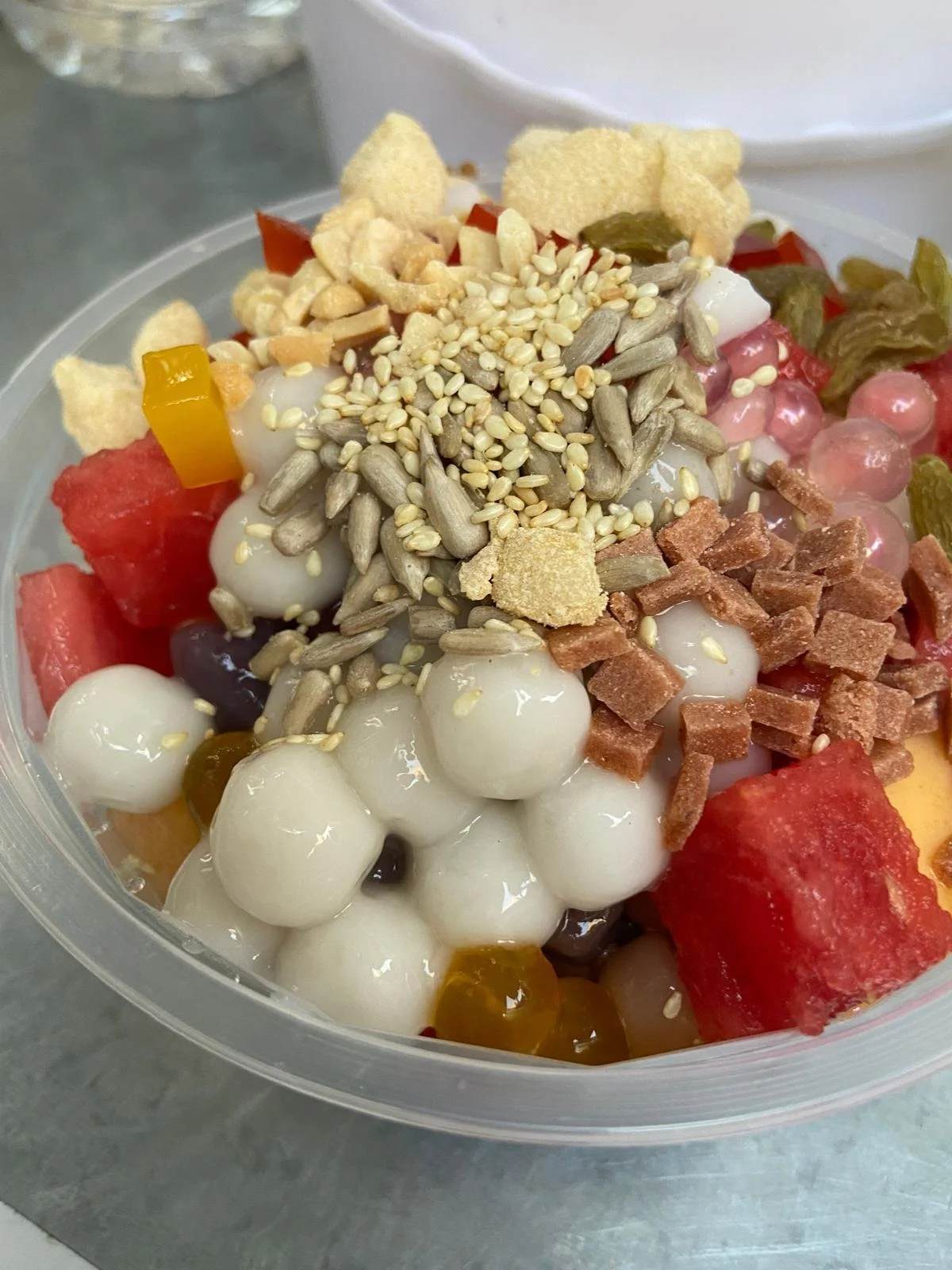 A bowl of Filipino halo-halo with shaved ice, colorful fruits, sweet beans, jellies, topped with seeds and crunchy toppings.