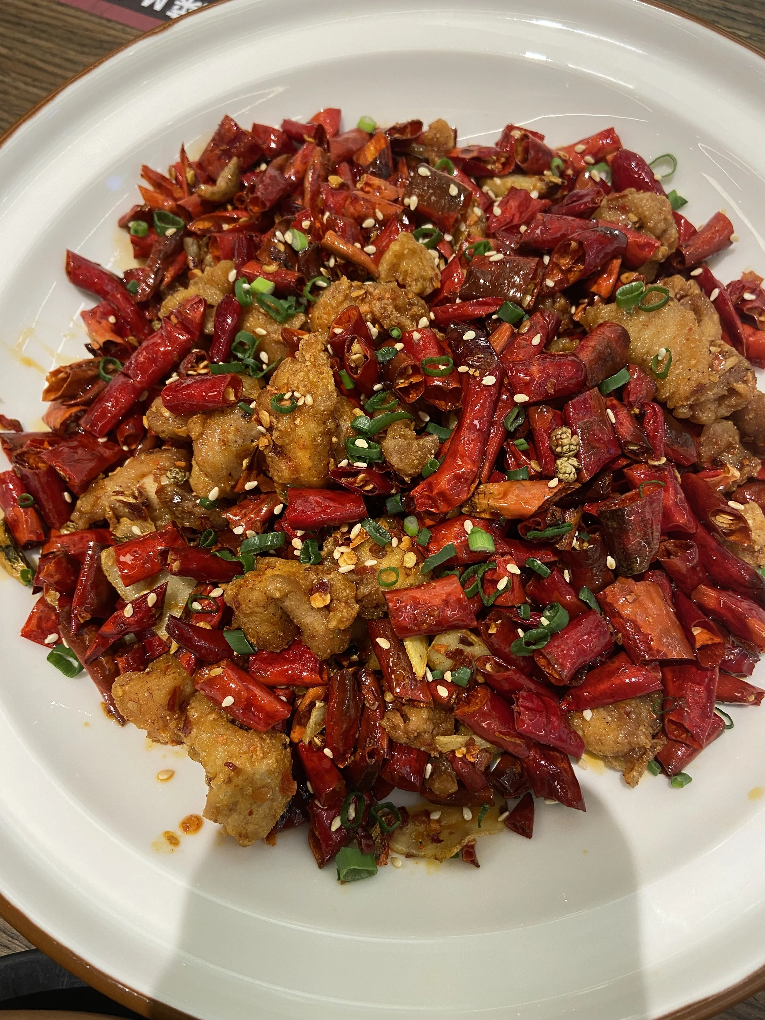 Plate of crispy fried chicken pieces topped with chopped red chili peppers, sliced green onions, and sesame seeds.