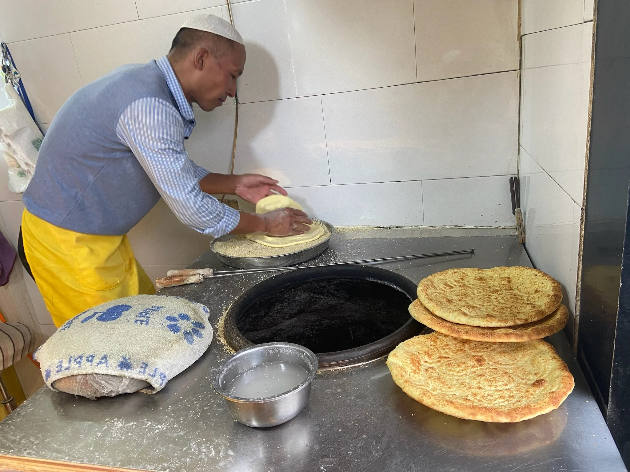 Man preparing flatbread in a kitchen with freshly baked bread on the countertop.
