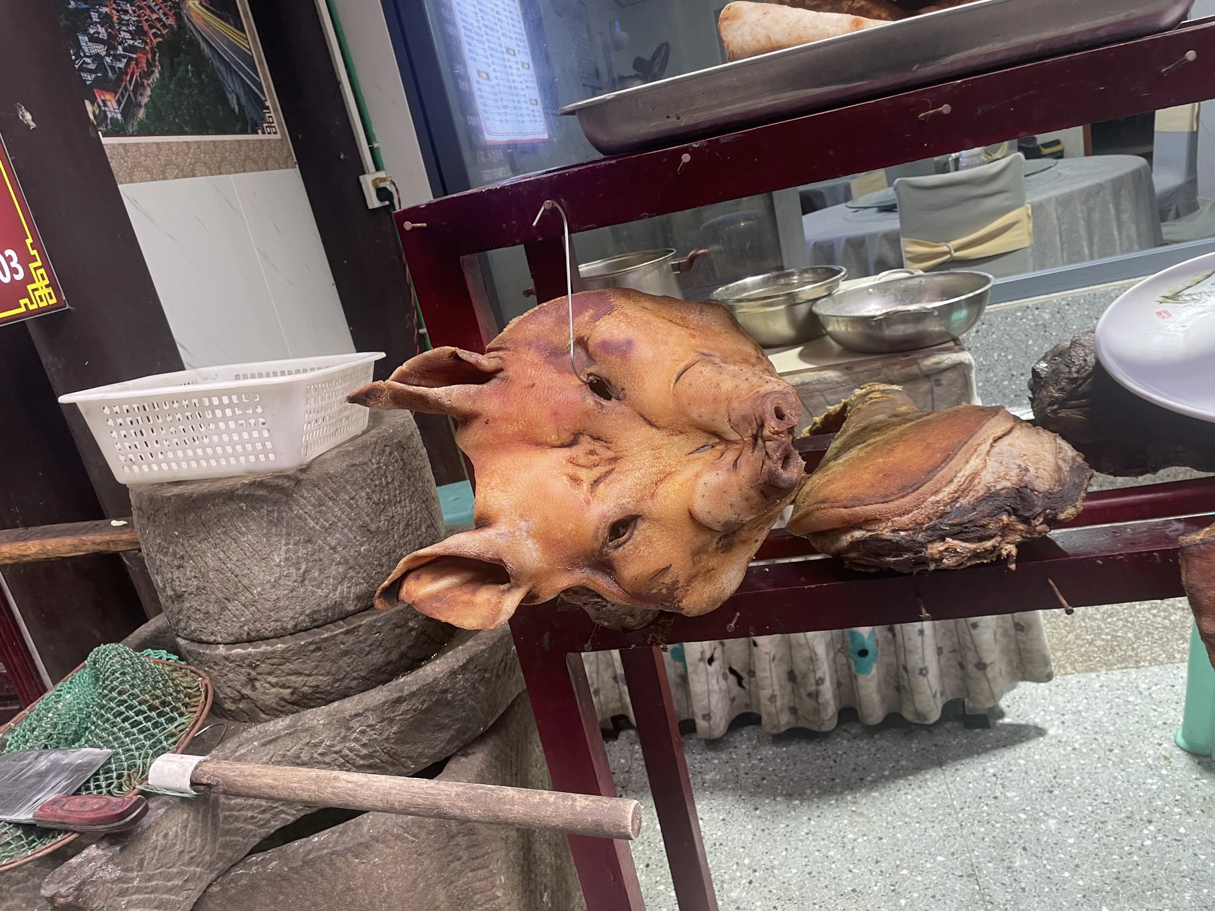 A pig's head and a large piece of meat displayed on a table in a restaurant kitchen.