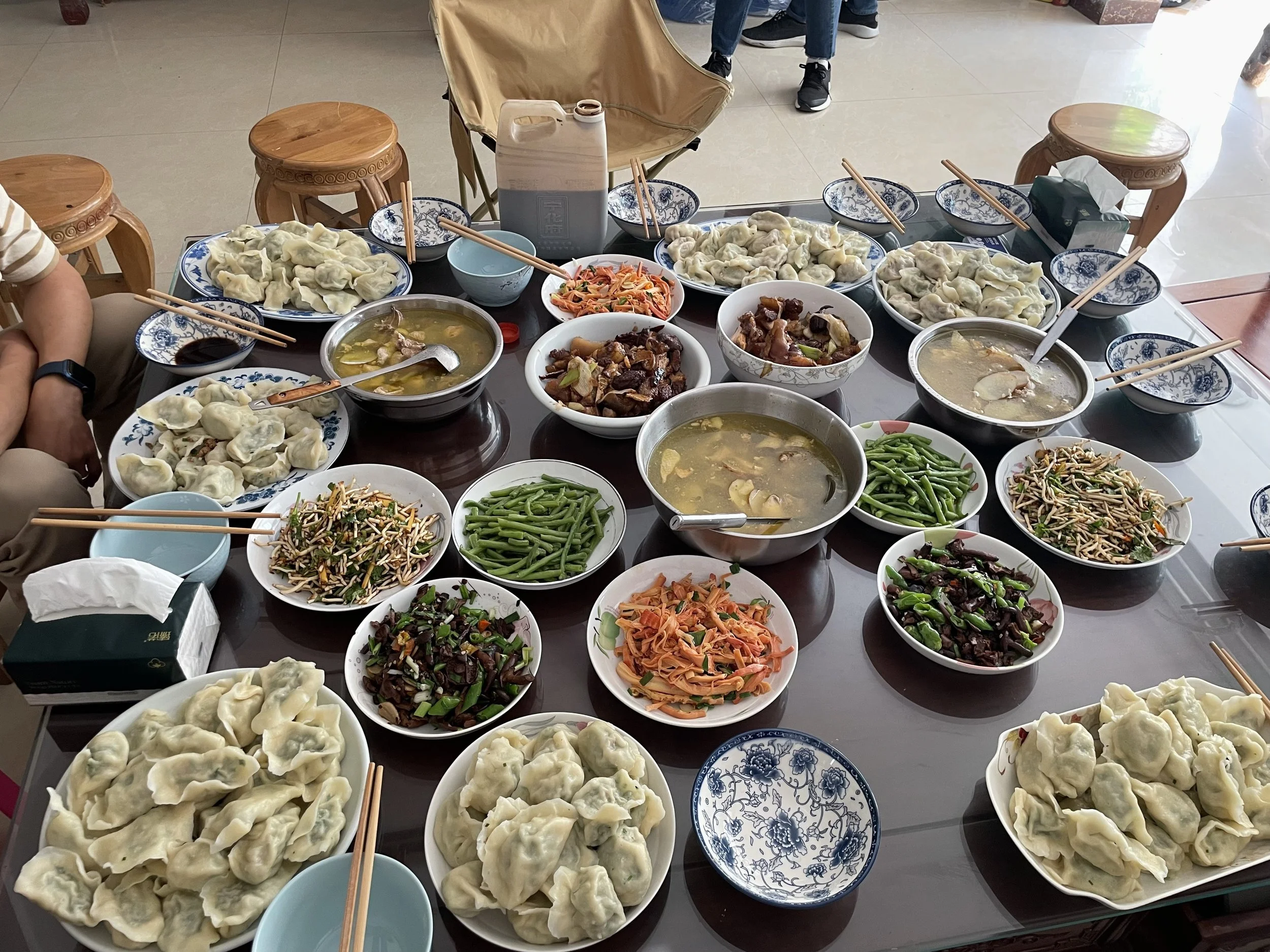A large table filled with various Chinese dishes including dumplings, soups, stir-fried vegetables, and meats, set for a communal meal.