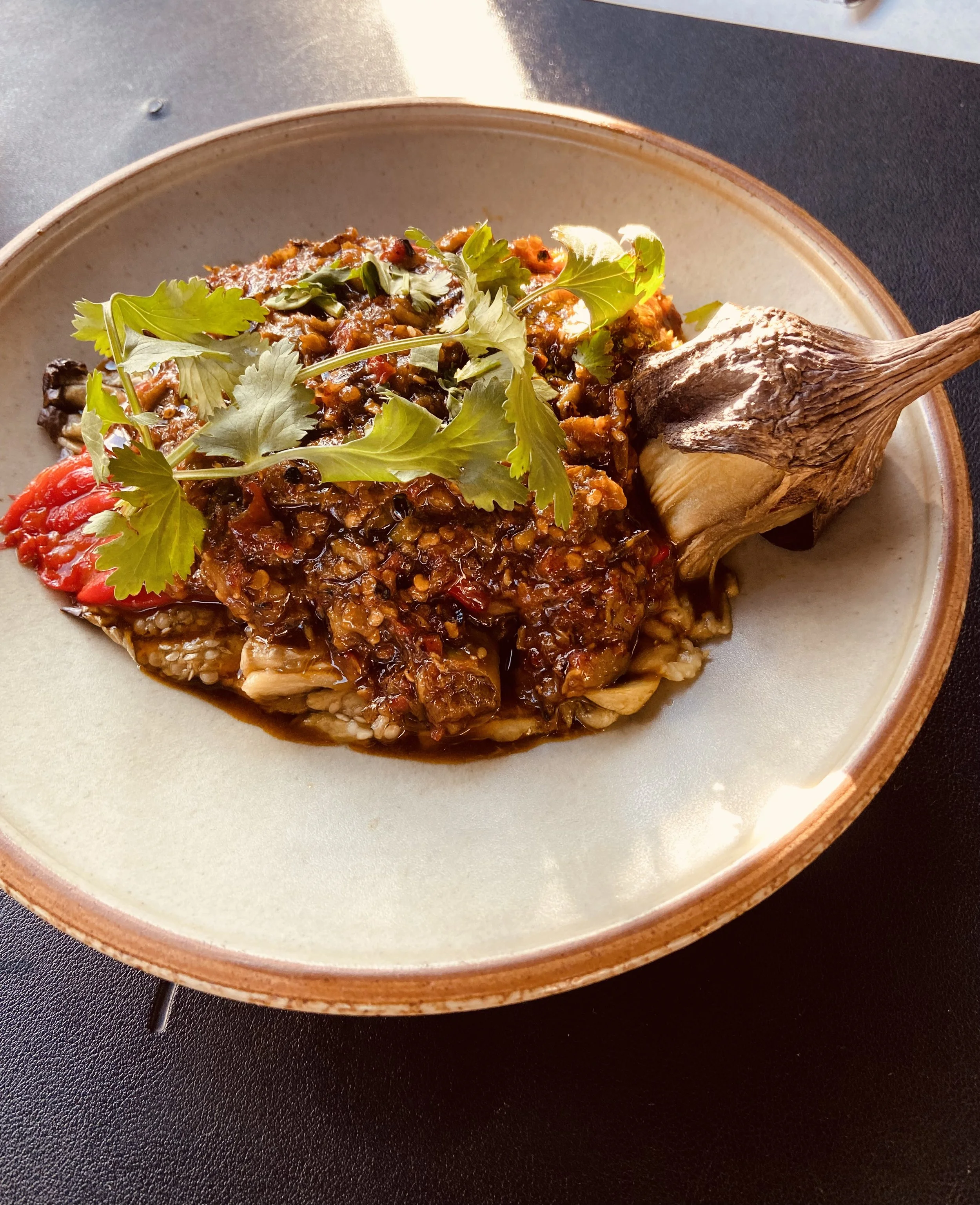 A plate of cooked meat topped with sauce, garnished with cilantro, and served with a roasted garlic bulb on the side.