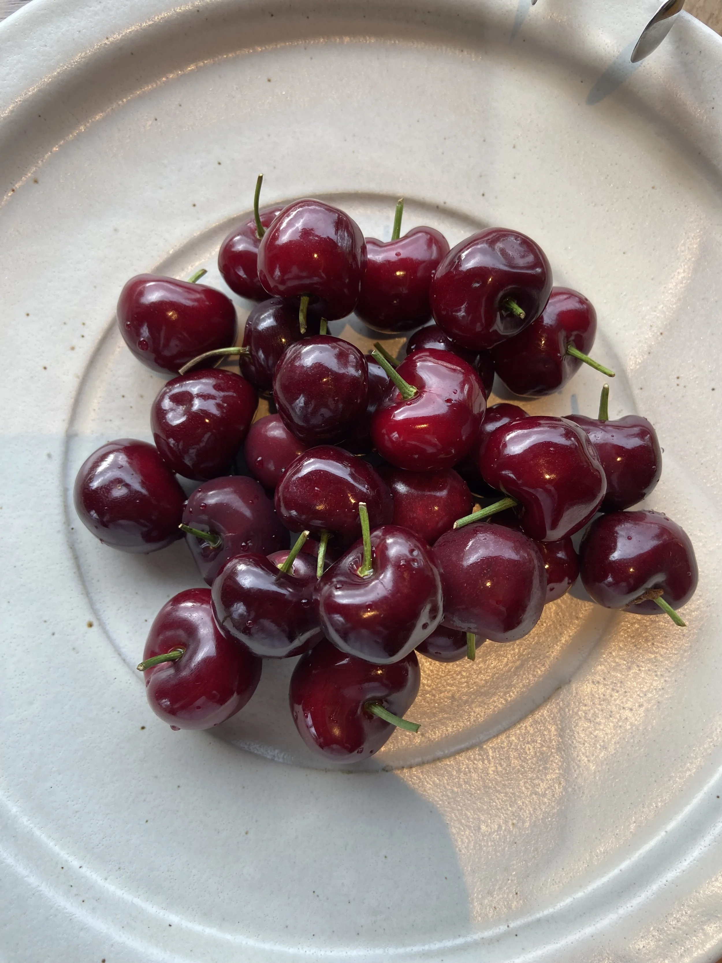 A cluster of ripe red cherries on a white plate.