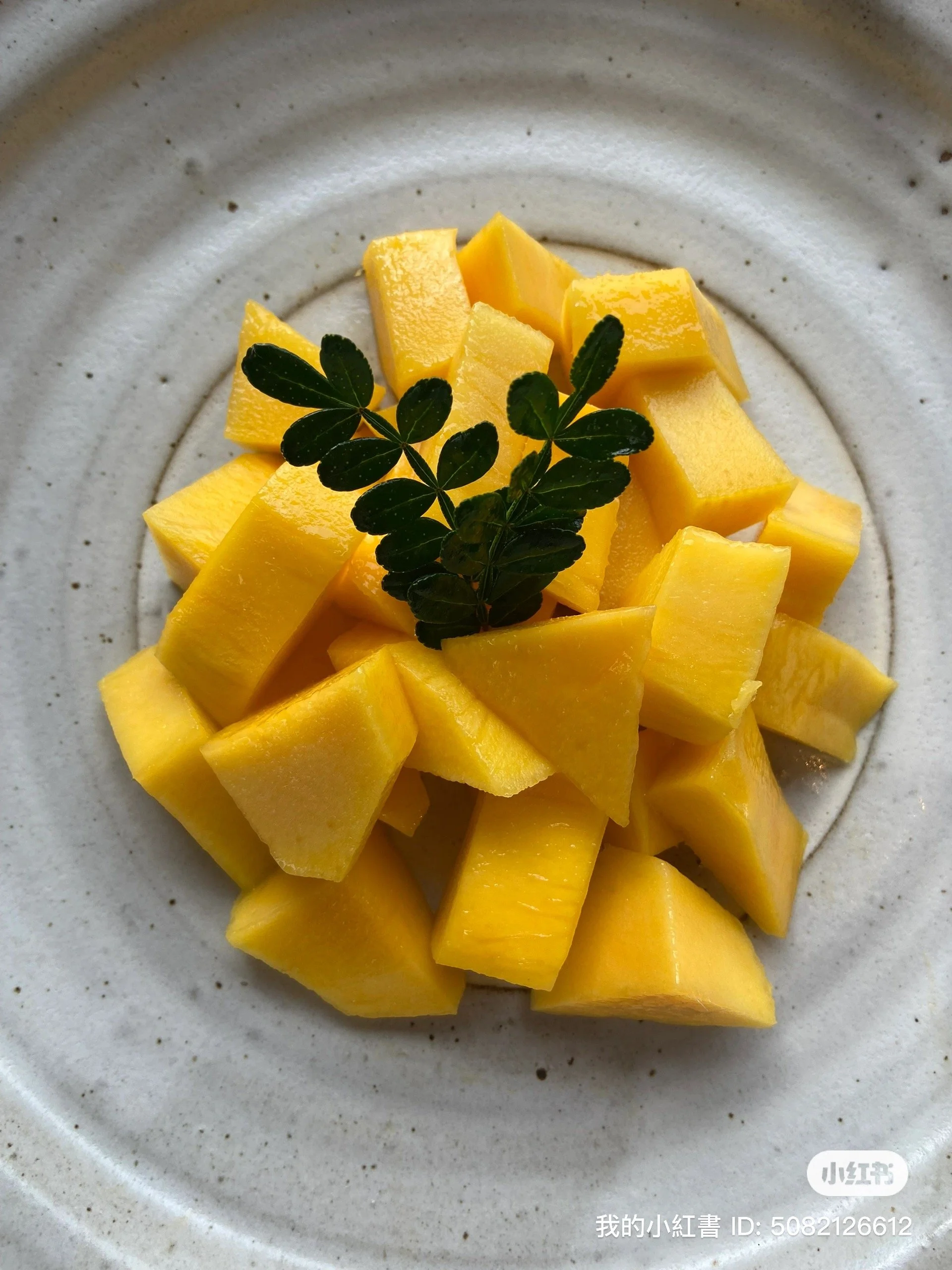 A white plate with chopped mango pieces and a small green herb sprig in the center.