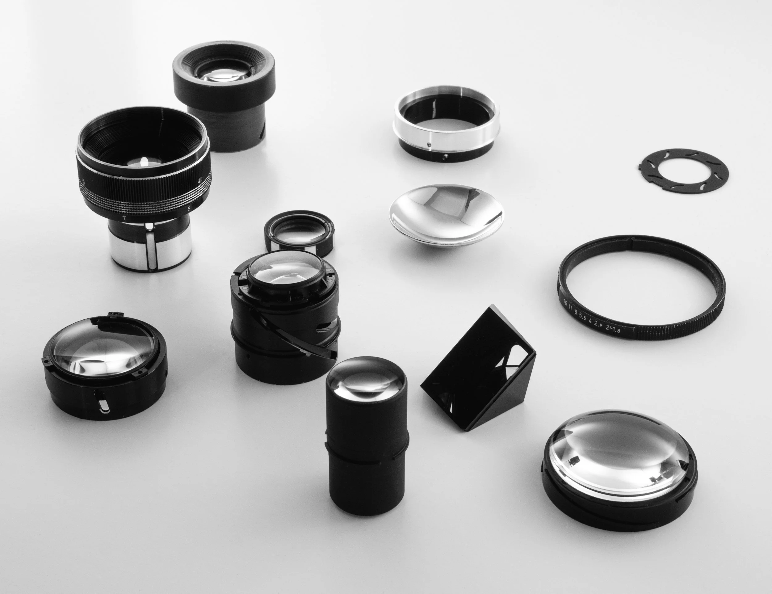 Various camera lenses and lens parts arranged on a white surface.