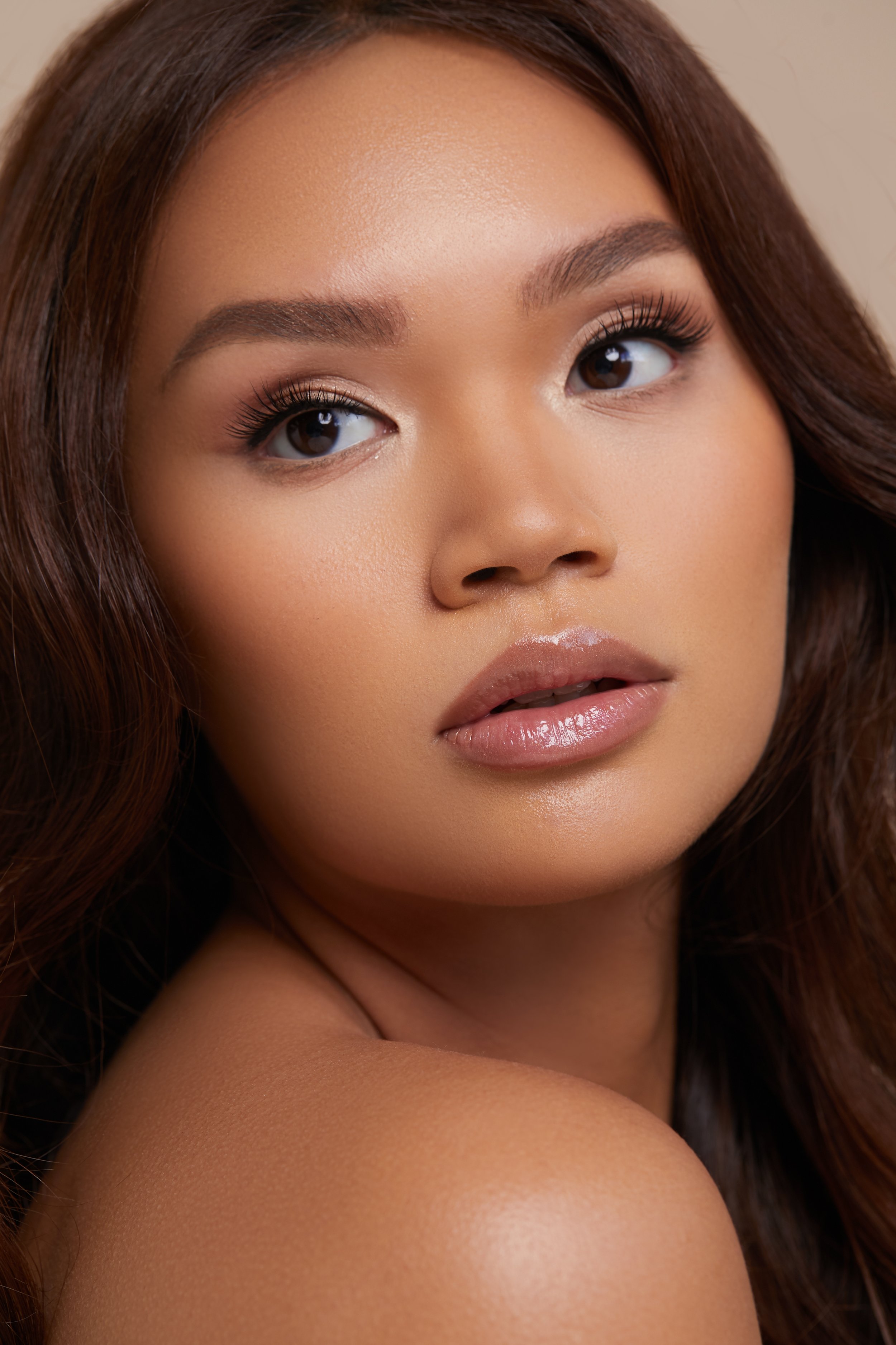 Beauty portrait of an Asian model with soft makeup, defined brows and glossy nude lips.