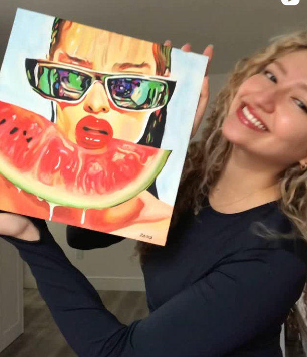 Woman smiling and holding a colorful painting of a woman with sunglasses and bright red lips eating a slice of watermelon.