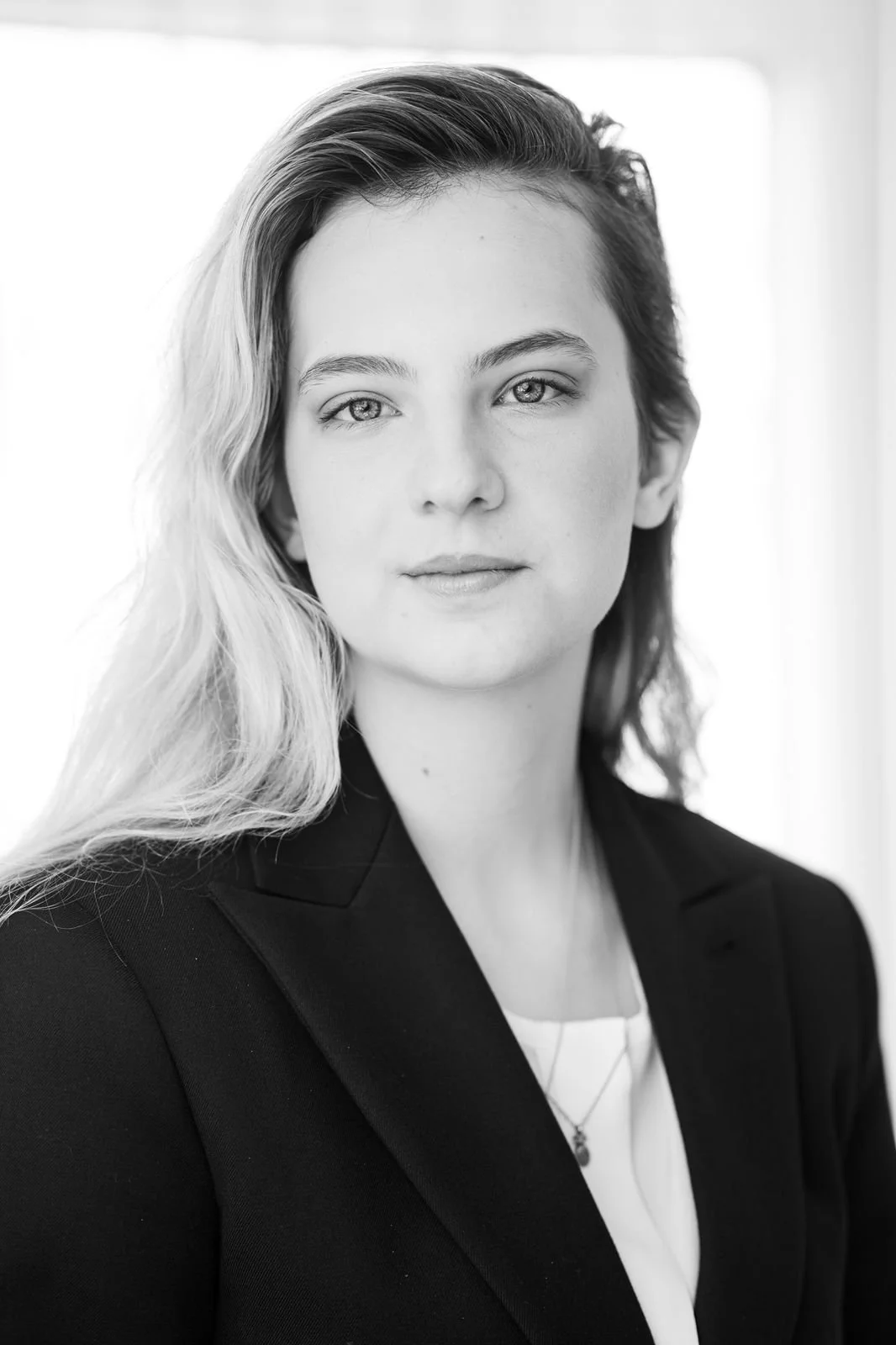 Black and white portrait of a woman with light wavy hair, wearing a dark blazer and light blouse, looking directly at the camera.