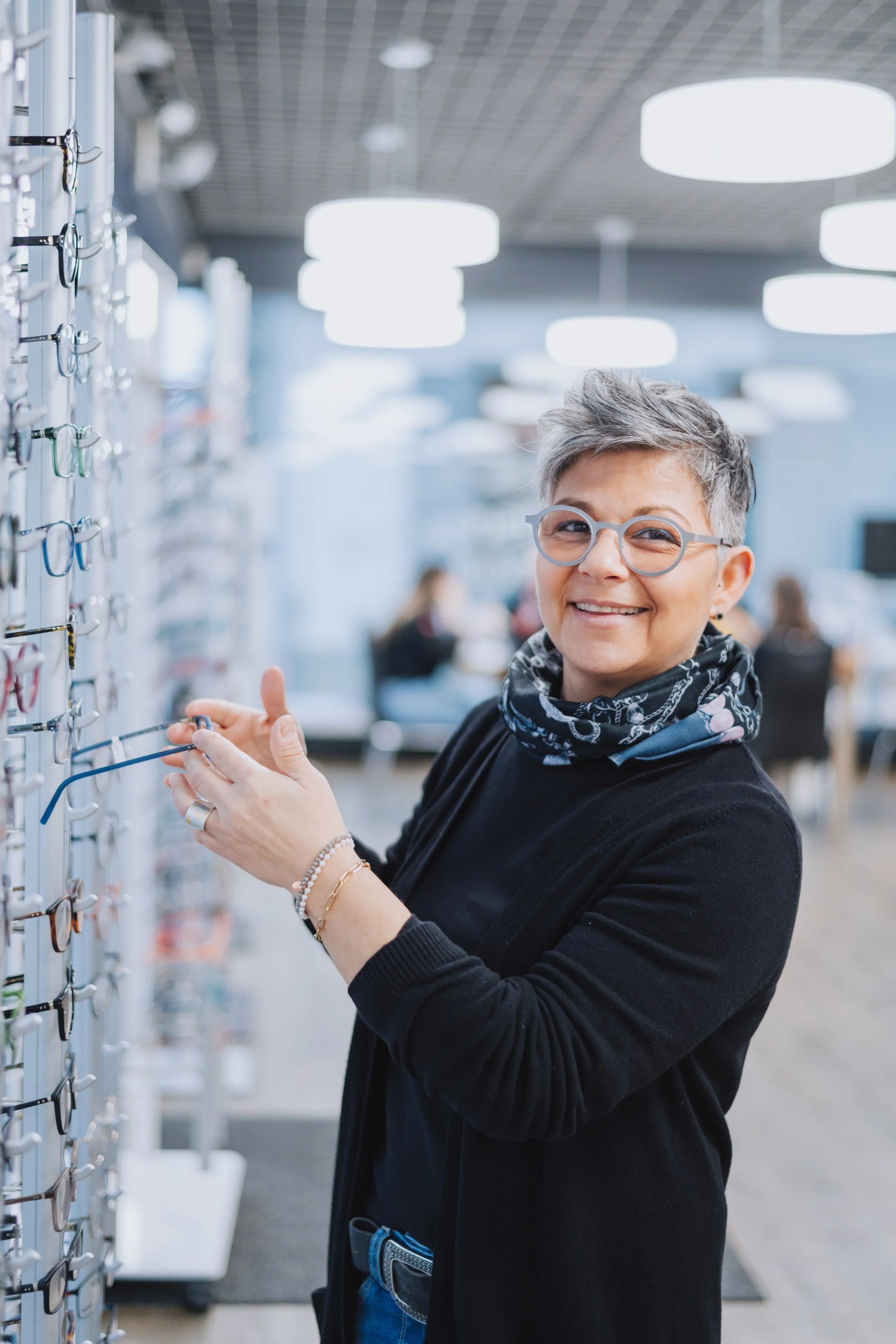 Frau lächelt beim Ausprobieren von Brillen in einem Optikgeschäft.