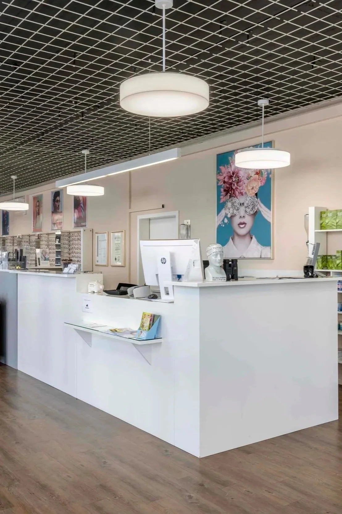 Rezeption in einem modernen Geschäft oder einer Klinik mit weißen Möbeln und überhängenden weißen Lampen, große Wandkunst mit einer Frau mit Blumen und Sonnenbrille, Holzfußboden.