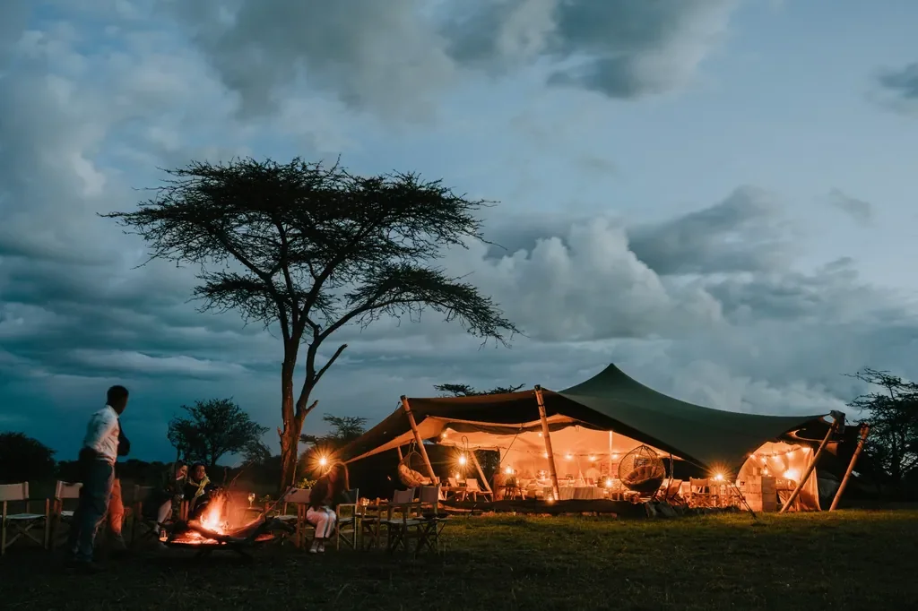 Usawa camp firepit and lantern lit stretch tent at dusk in Serengeti National Park