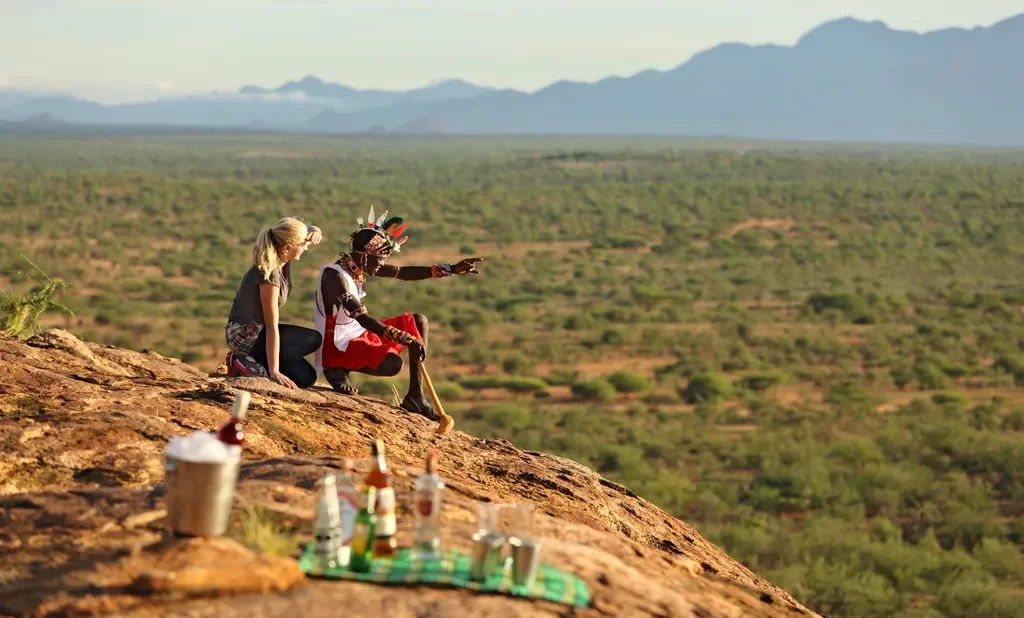 Guide and guest at Sasaab sundowner lookout with sweeping Samburu plains and Mathews Range, Kenya