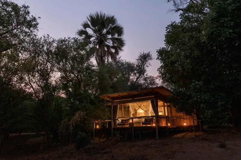 Little Ruckomechi tented suite exterior at dusk, private deck under palms near the Zambezi River, Mana Pools National Park, Zimbabwe