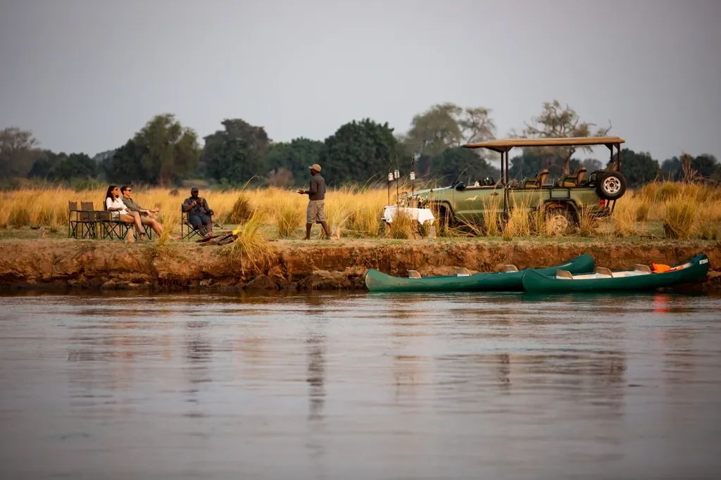 Riverside sundowners with safari vehicle and canoes near Little Ruckomechi, Zambezi River, Mana Pools, Zimbabwe