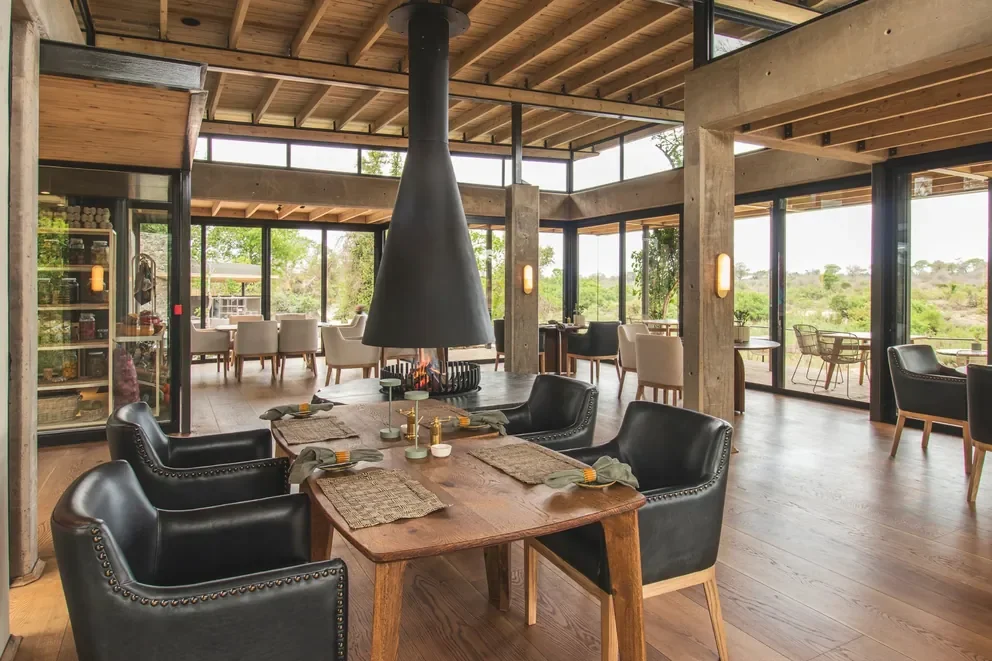 Elegant dining room at Lion Sands Ivory Lodge, Sabi Sand, Greater Kruger, South Africa with central fireplace and panoramic glass walls onto the bush