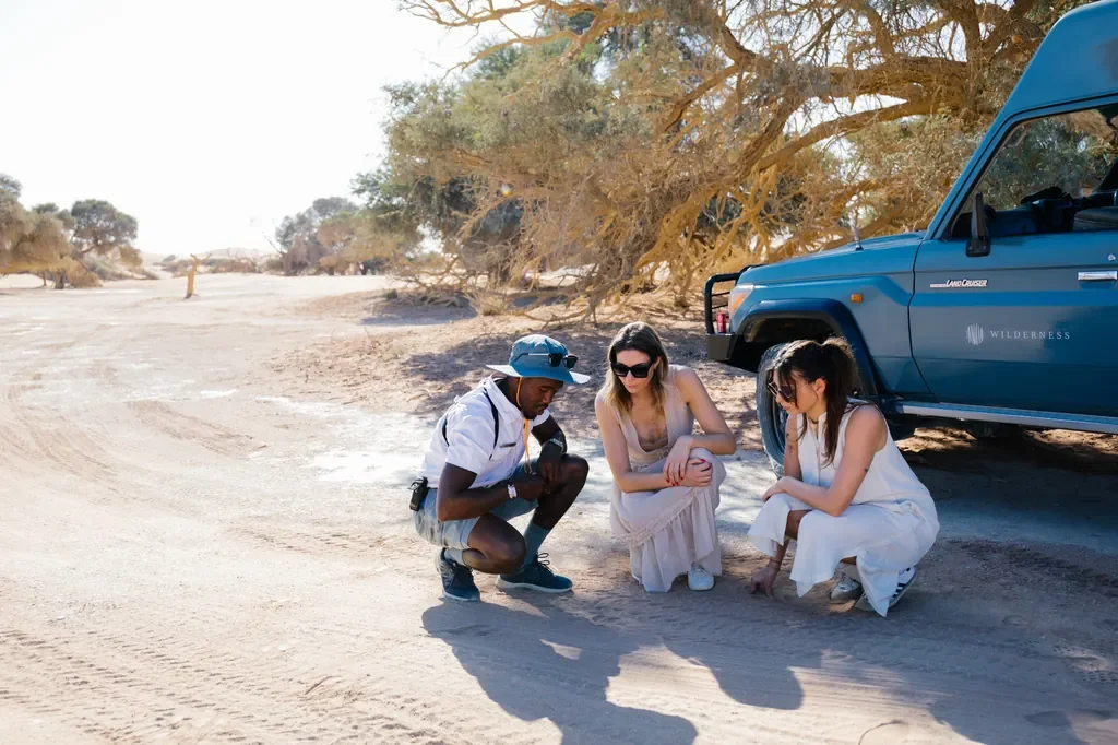Kulala Desert Lodge guide tracking wildlife with guests beside Land Cruiser in Sossusvlei, Namibia
