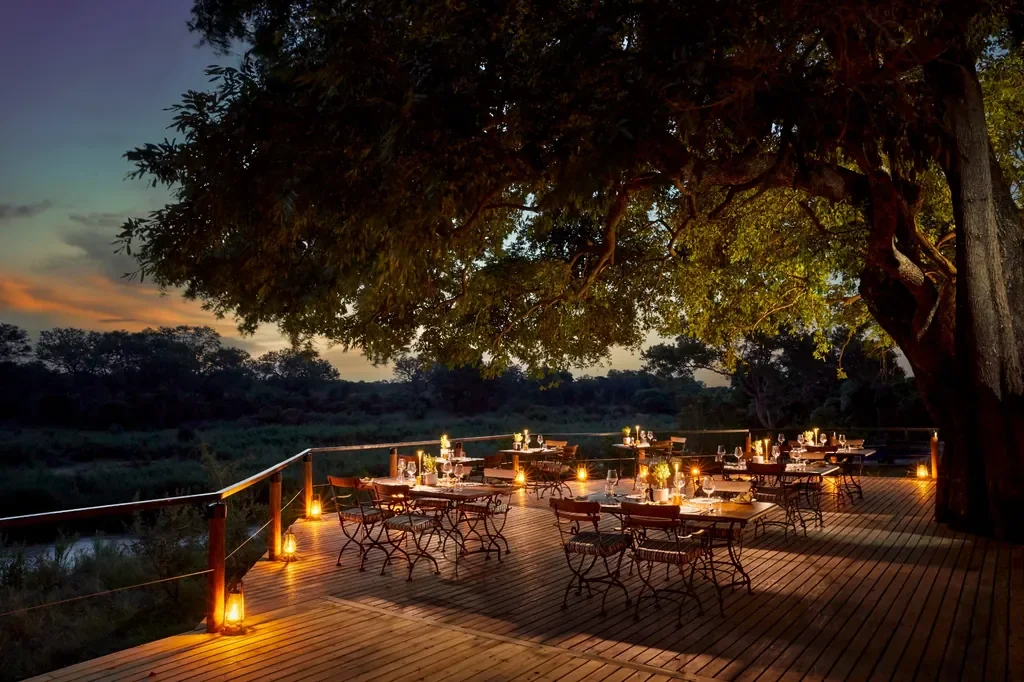 Signature river deck at Lion Sands Tinga Lodge lit for dinner, Sabi Sand, Greater Kruger